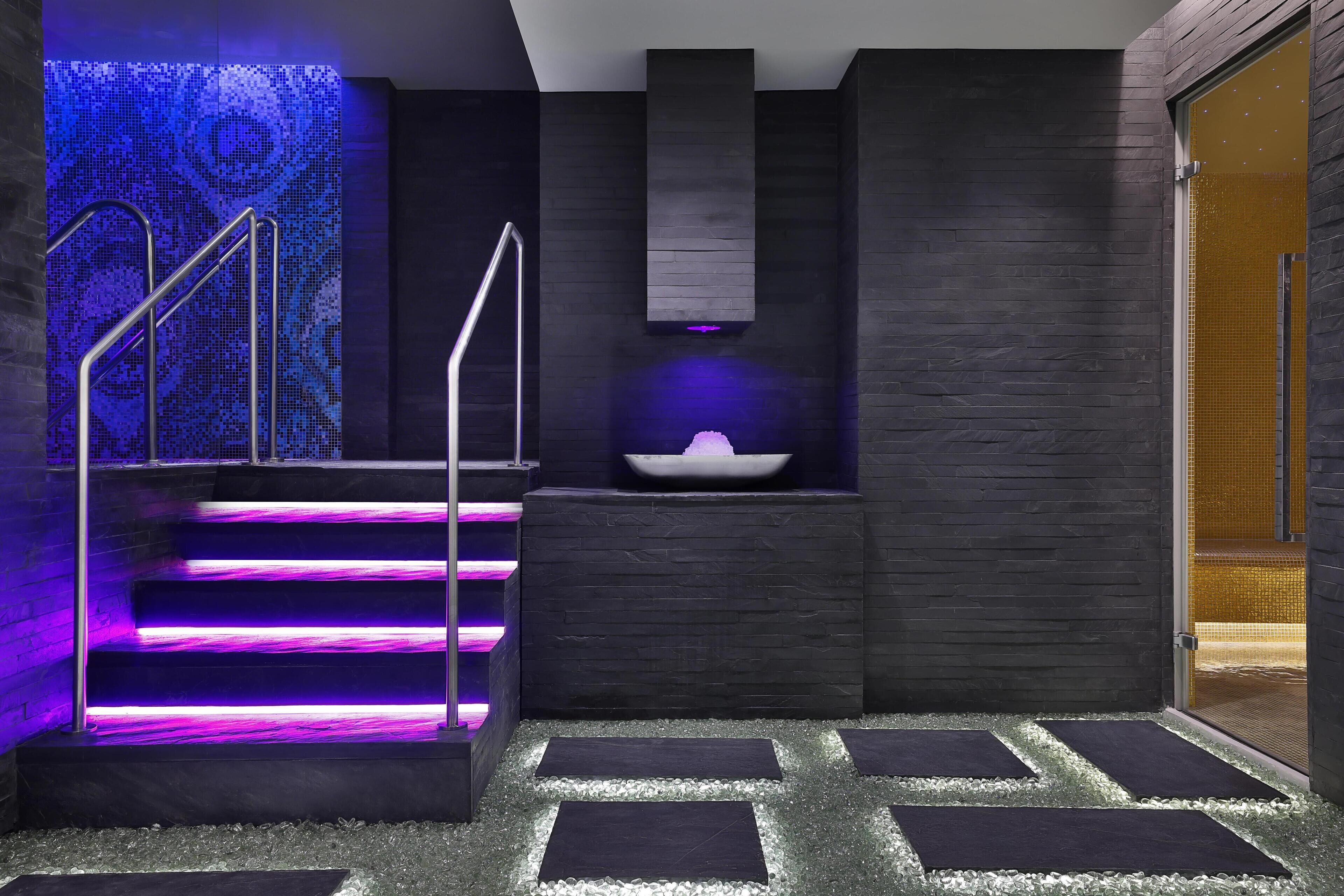 Een moderne badkamer met een zwart-wit betegelde muur, een ingebouwd wastafelmeubel en een paars verlichte trap.