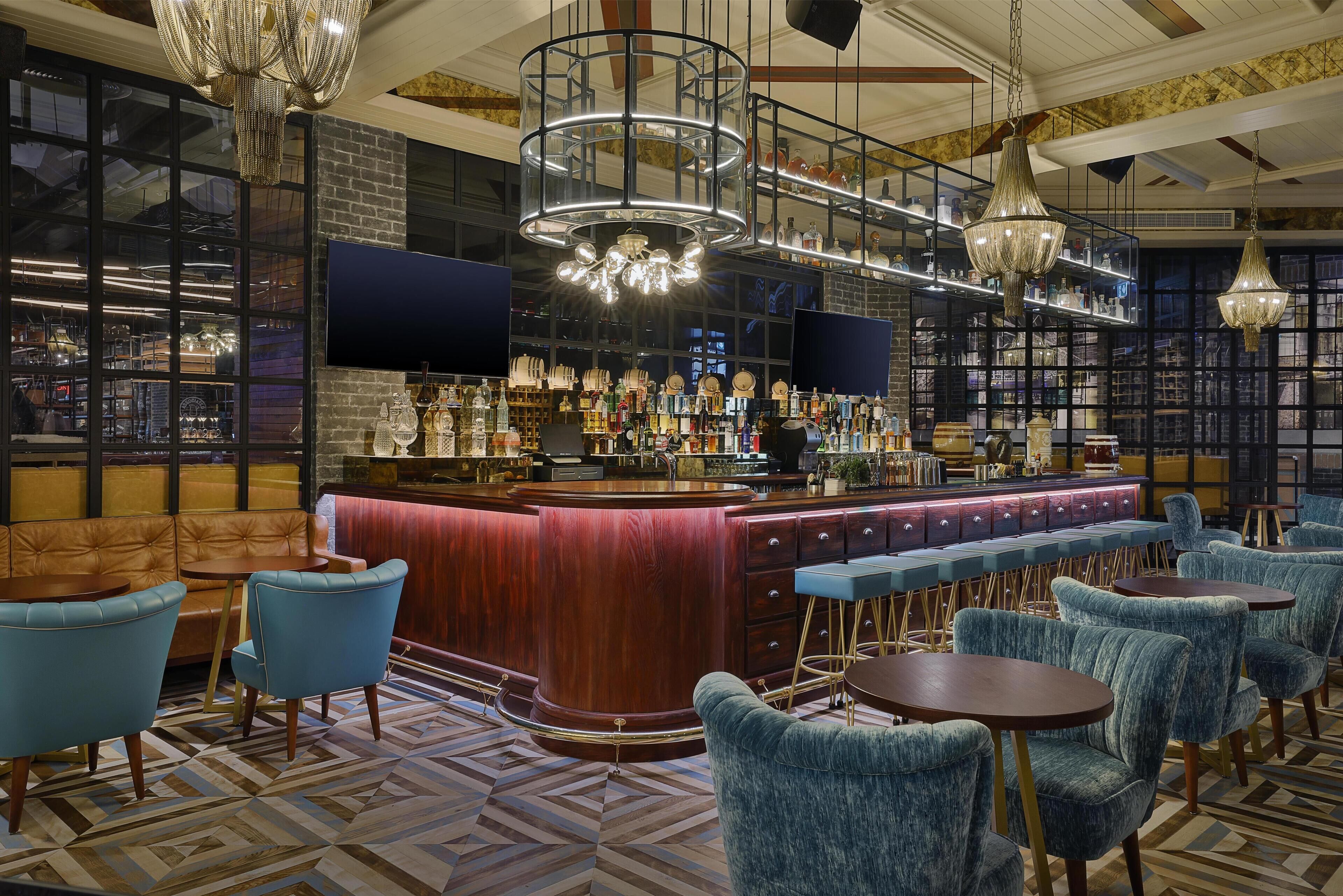Eine Bar mit einer Holztheke, blauen Stühlen und einem gemusterten Boden.