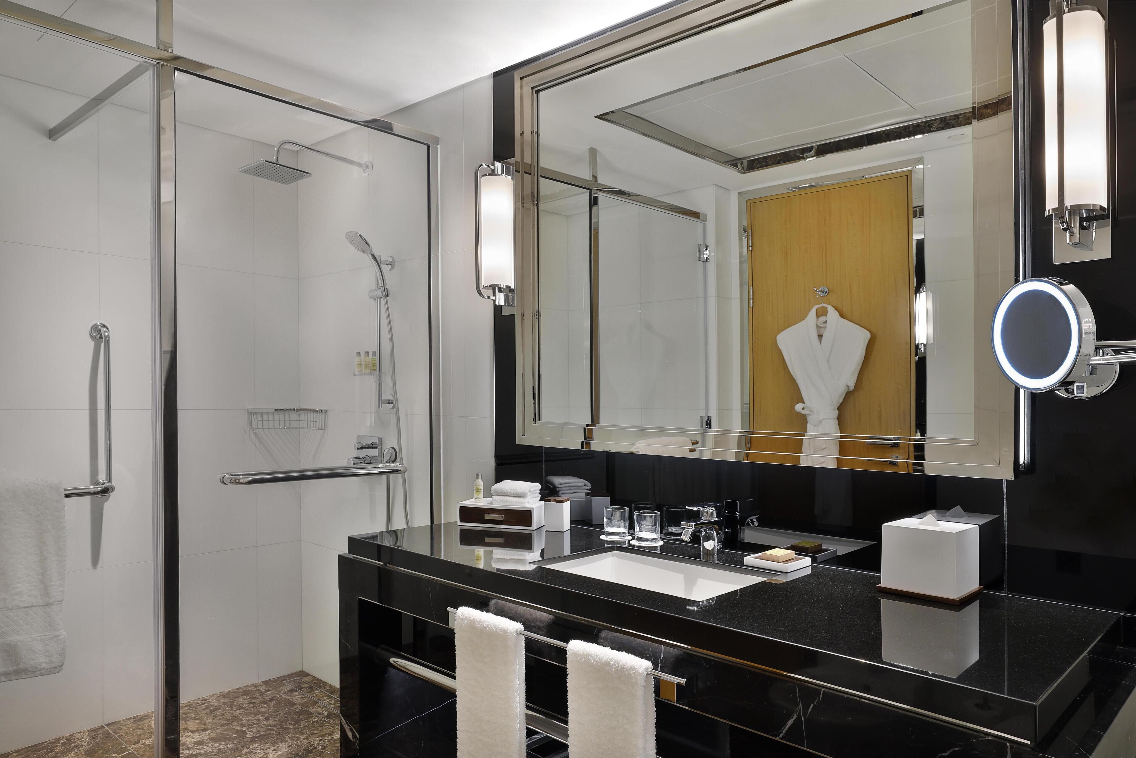 A modern bathroom with a glass-enclosed shower, a black vanity with a large mirror, and a white towel hanging on the wall.