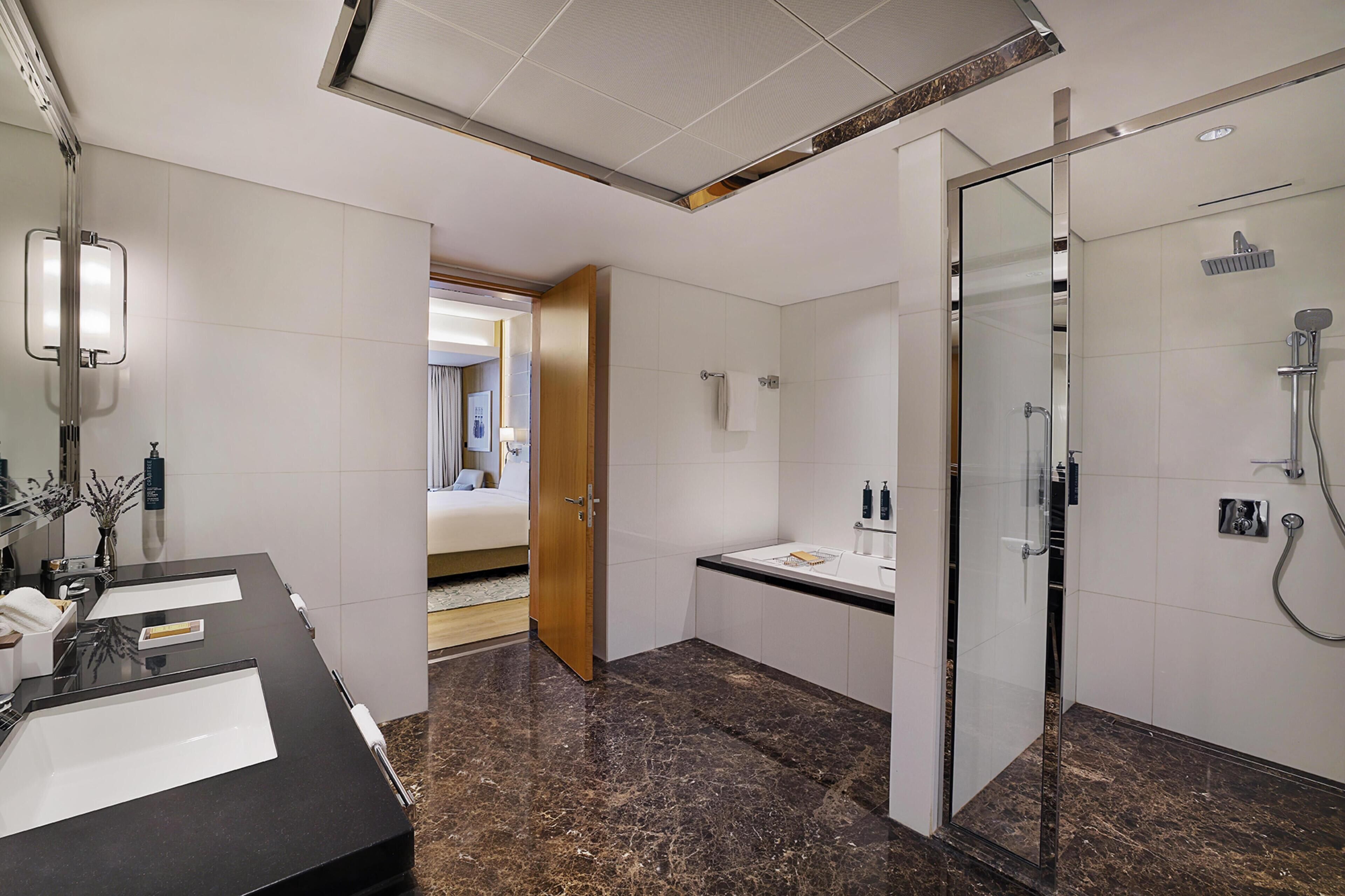 Uma casa de banho moderna com duas lavatórios, chuveiro e zona de duche com paredes de vidro.