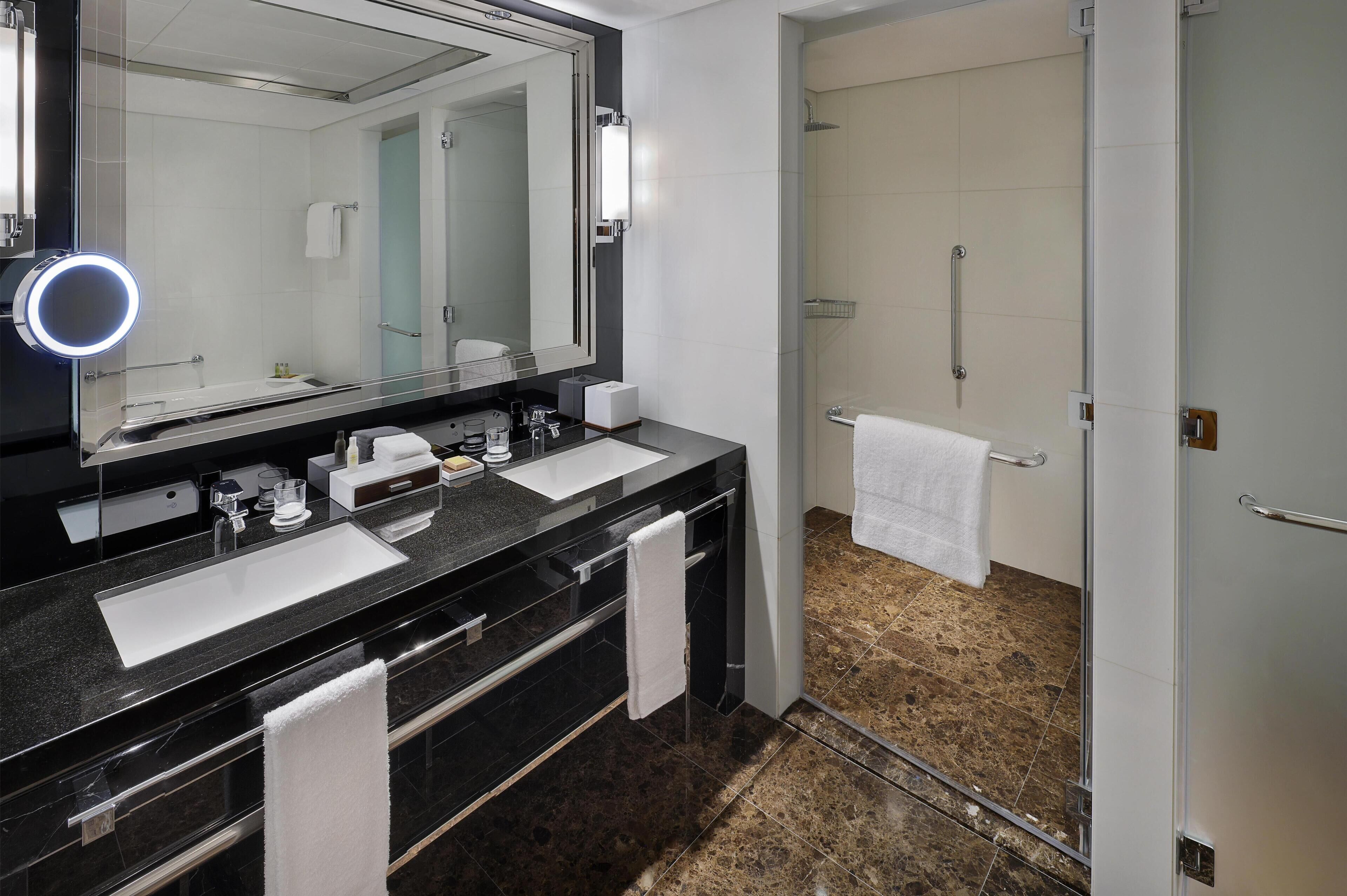 A modern bathroom with two sinks, a large mirror, and a glass-enclosed shower.