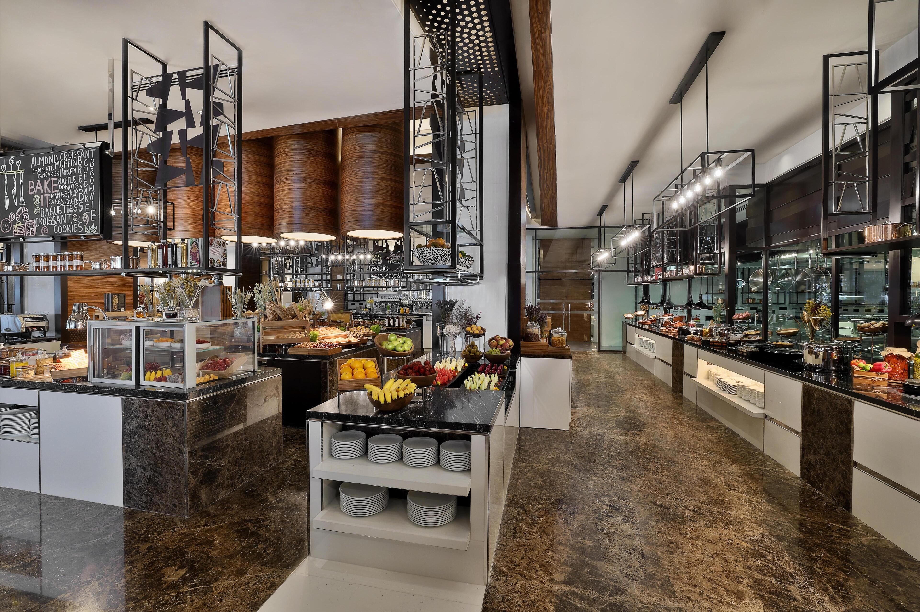 A modern kitchen with marble countertops, a variety of food items, and a central island with fruit bowls.