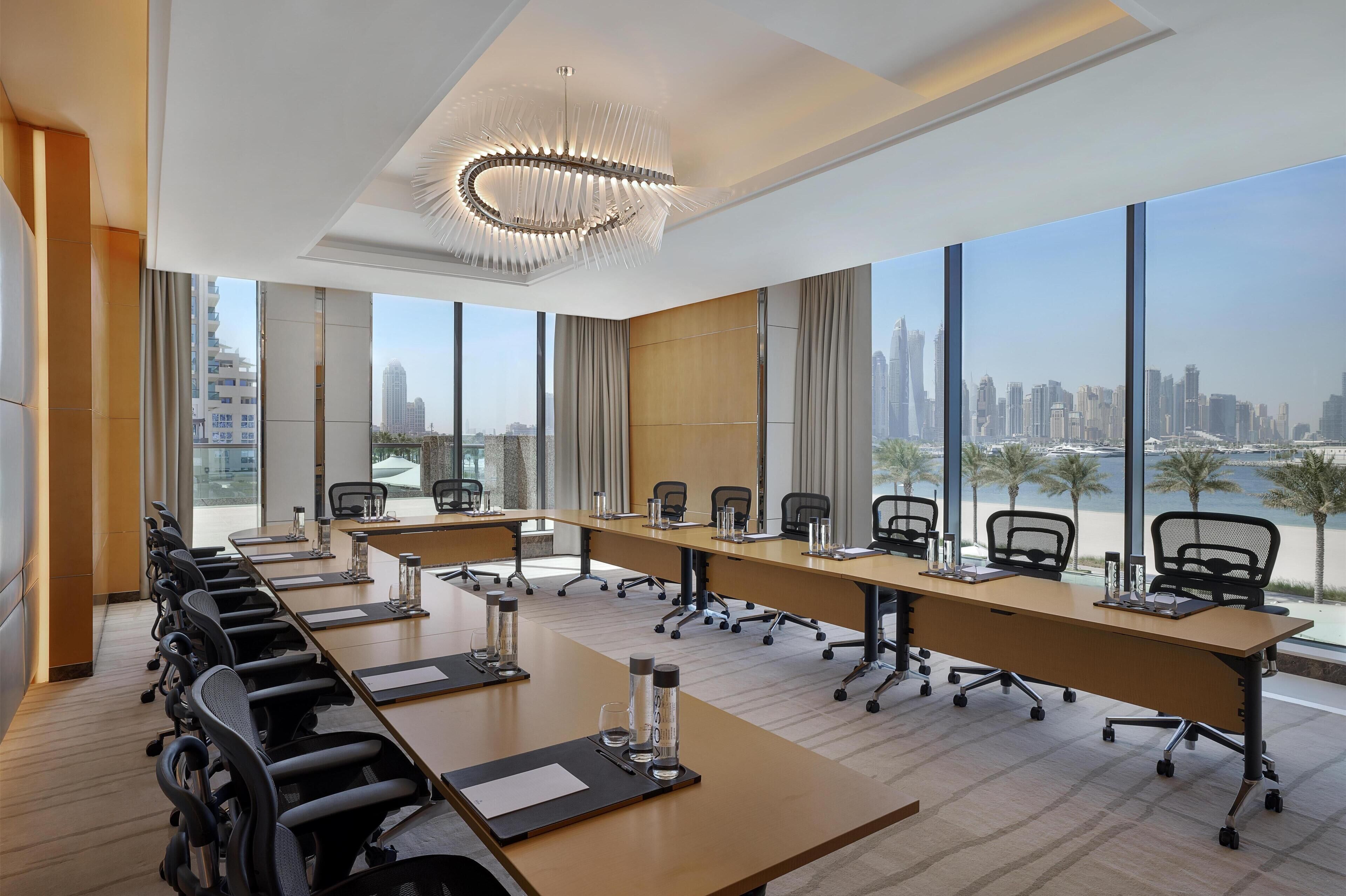 Una sala de conferencias moderna con una larga mesa, sillas y ventanas amplias que dan a vistas de la ciudad.