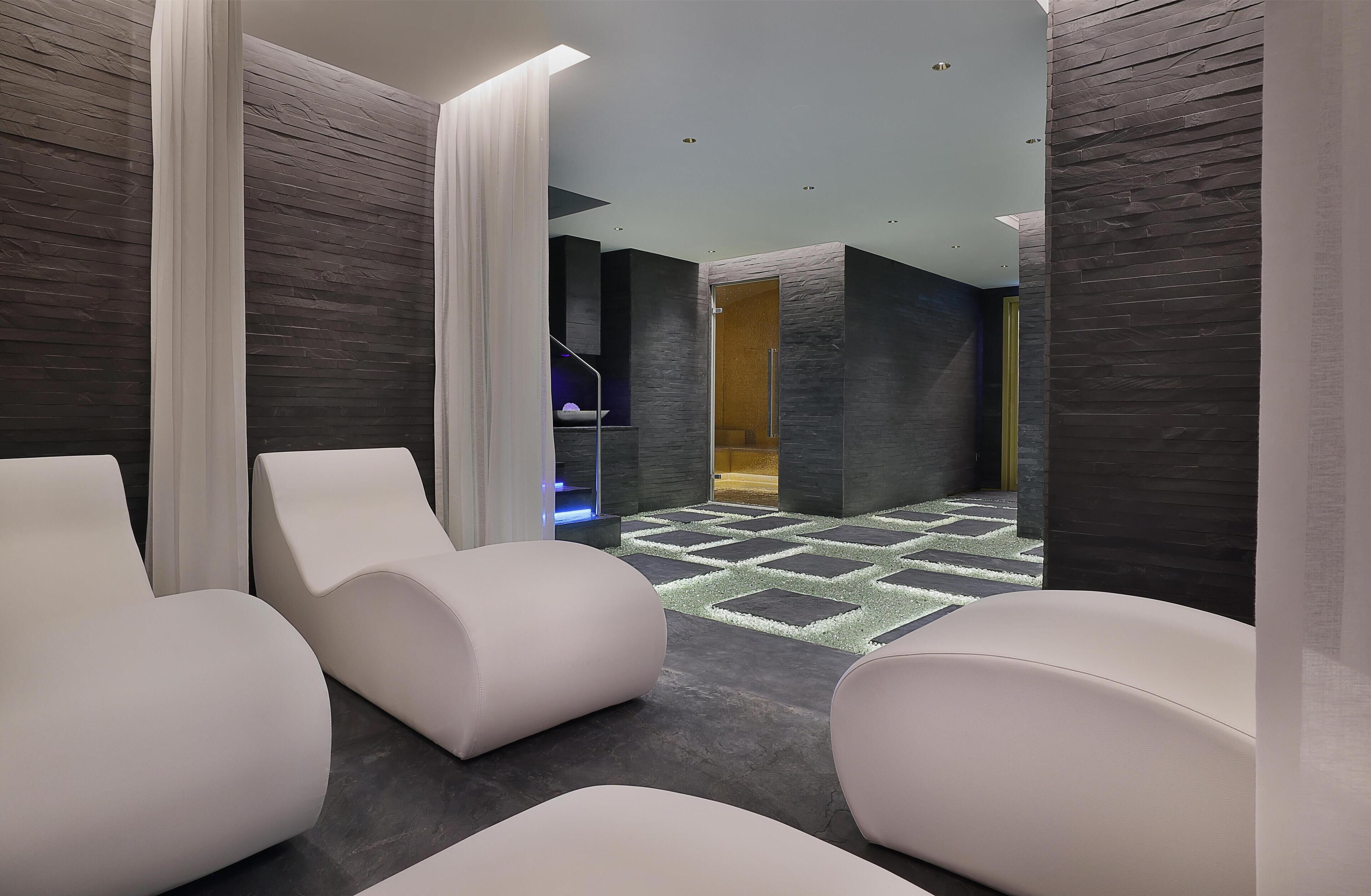 A modern spa area with white cushioned chairs, a patterned floor, and dark stone walls.