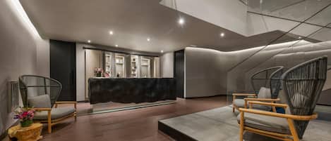 A modern lobby with a reception desk, wicker chairs, and a wooden floor.