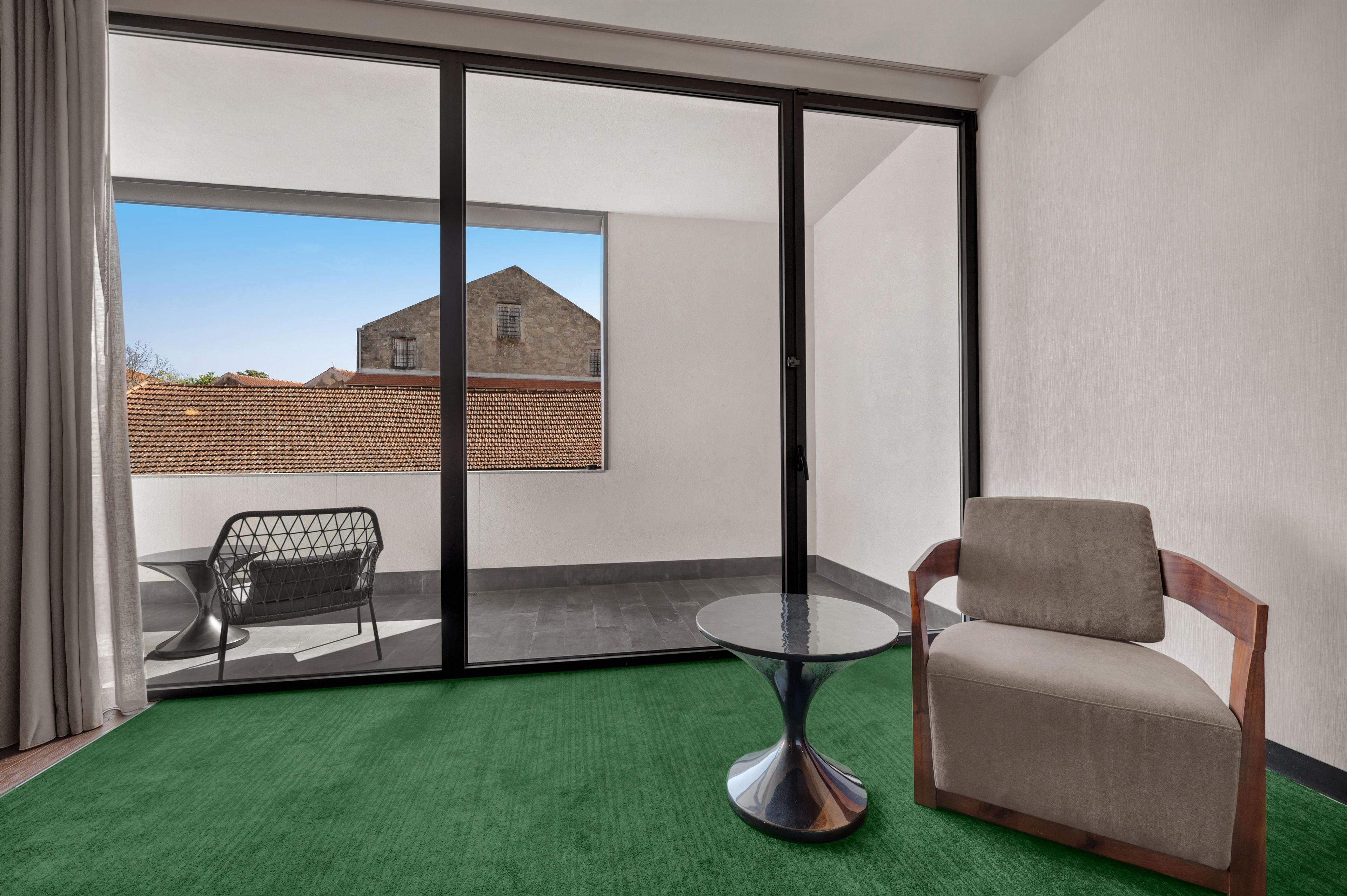 A room with a sliding glass door leading to a terrace, a round table with a chair, and a sofa.