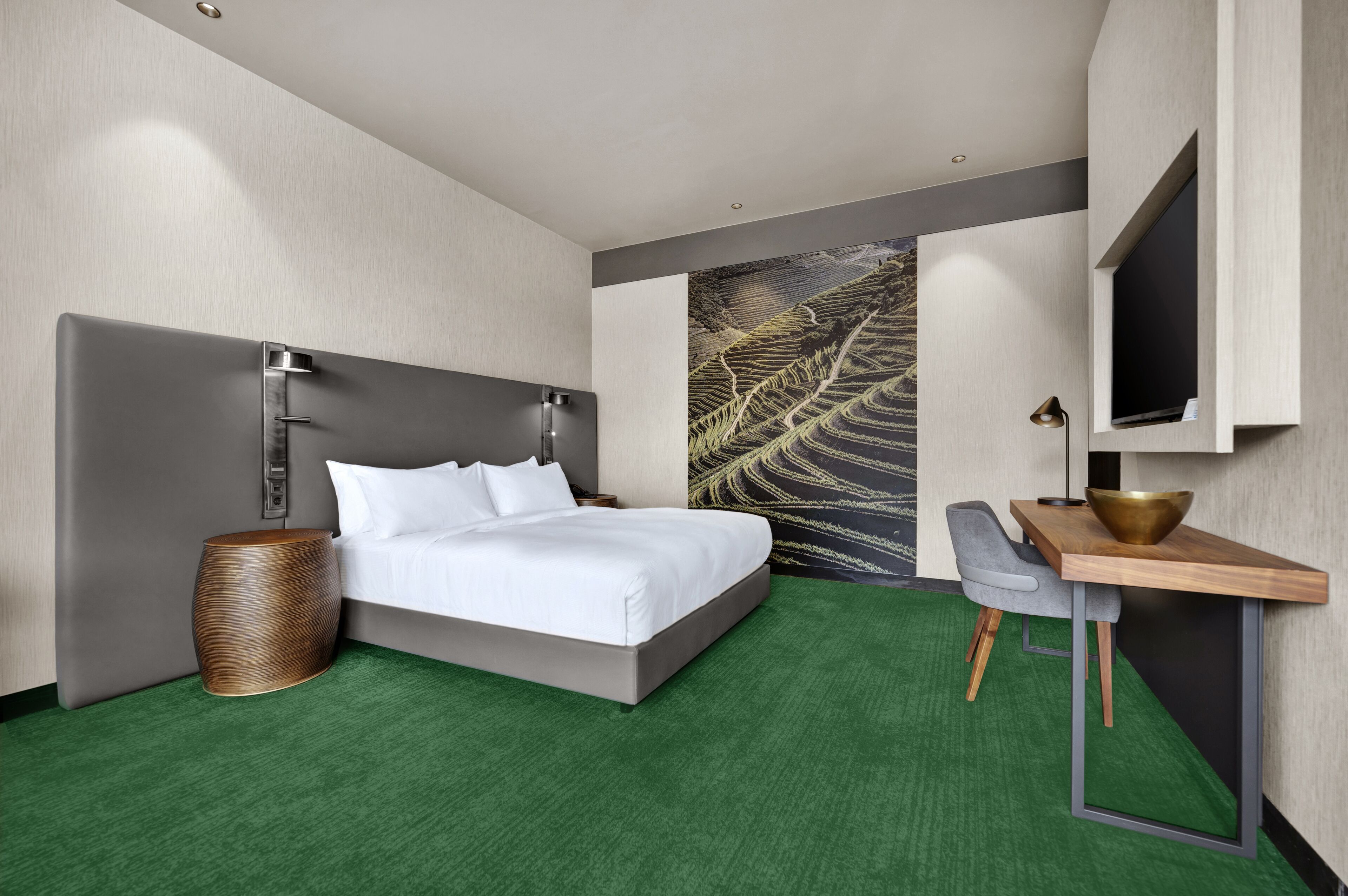 Een moderne hotelkamer met een groot bed, een bureau met een schaal, een stoel en een aan de muur bevestigde televisie.