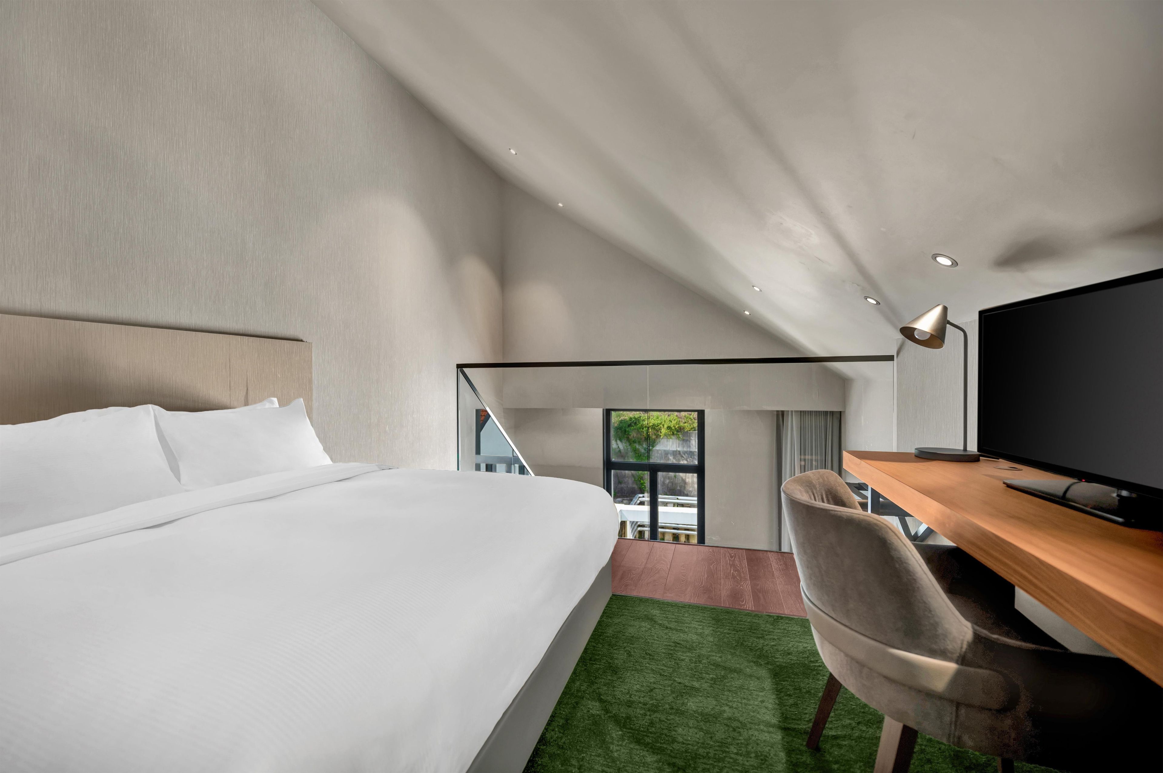 A modern hotel room with a large bed, a desk with a flat-screen TV, and a view of the outdoors.