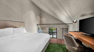 A modern hotel room with a large bed, a desk with a flat-screen TV, and a view of the outdoors.