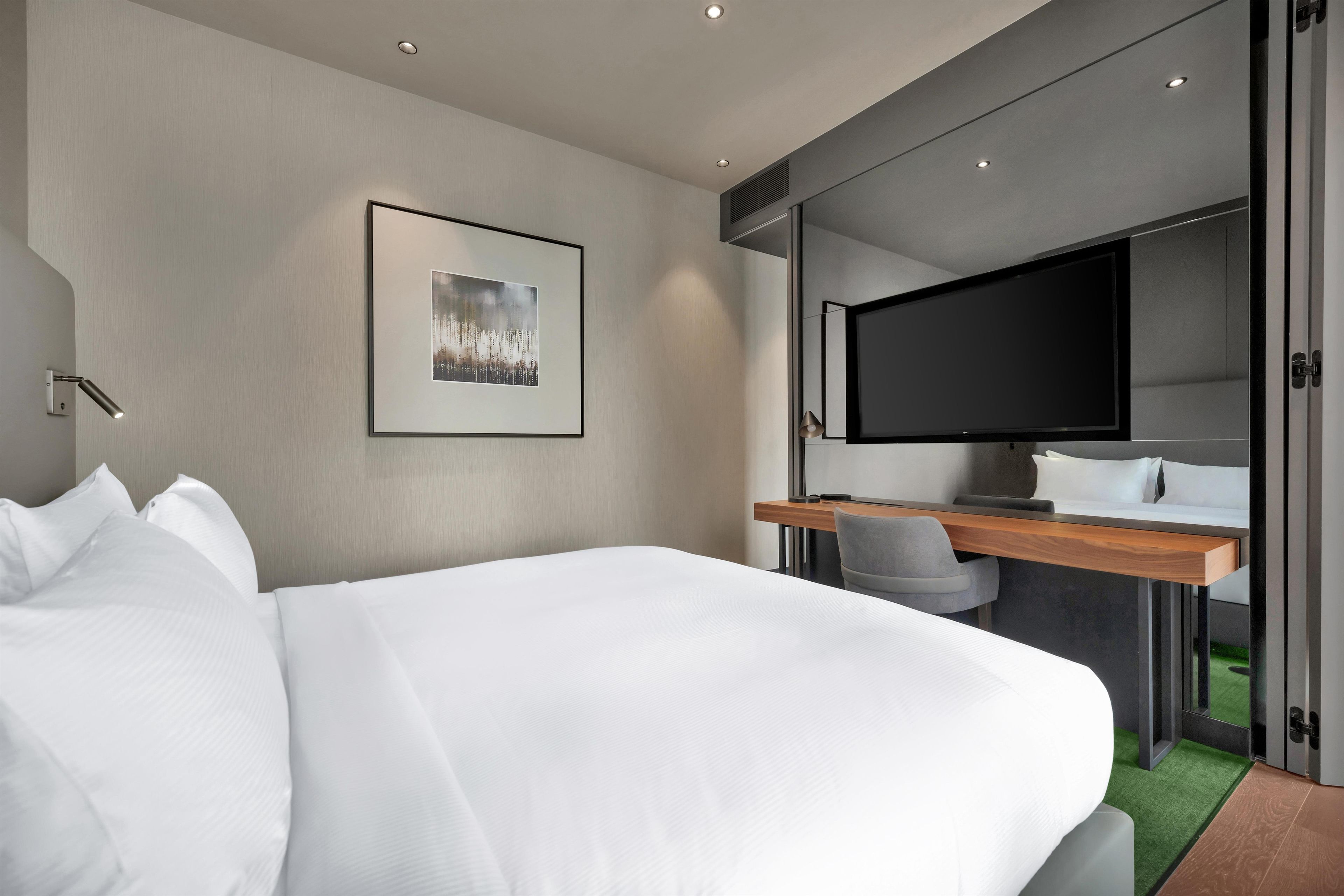 A modern hotel room with a large bed, a desk with a flat-screen TV, and a large mirror.