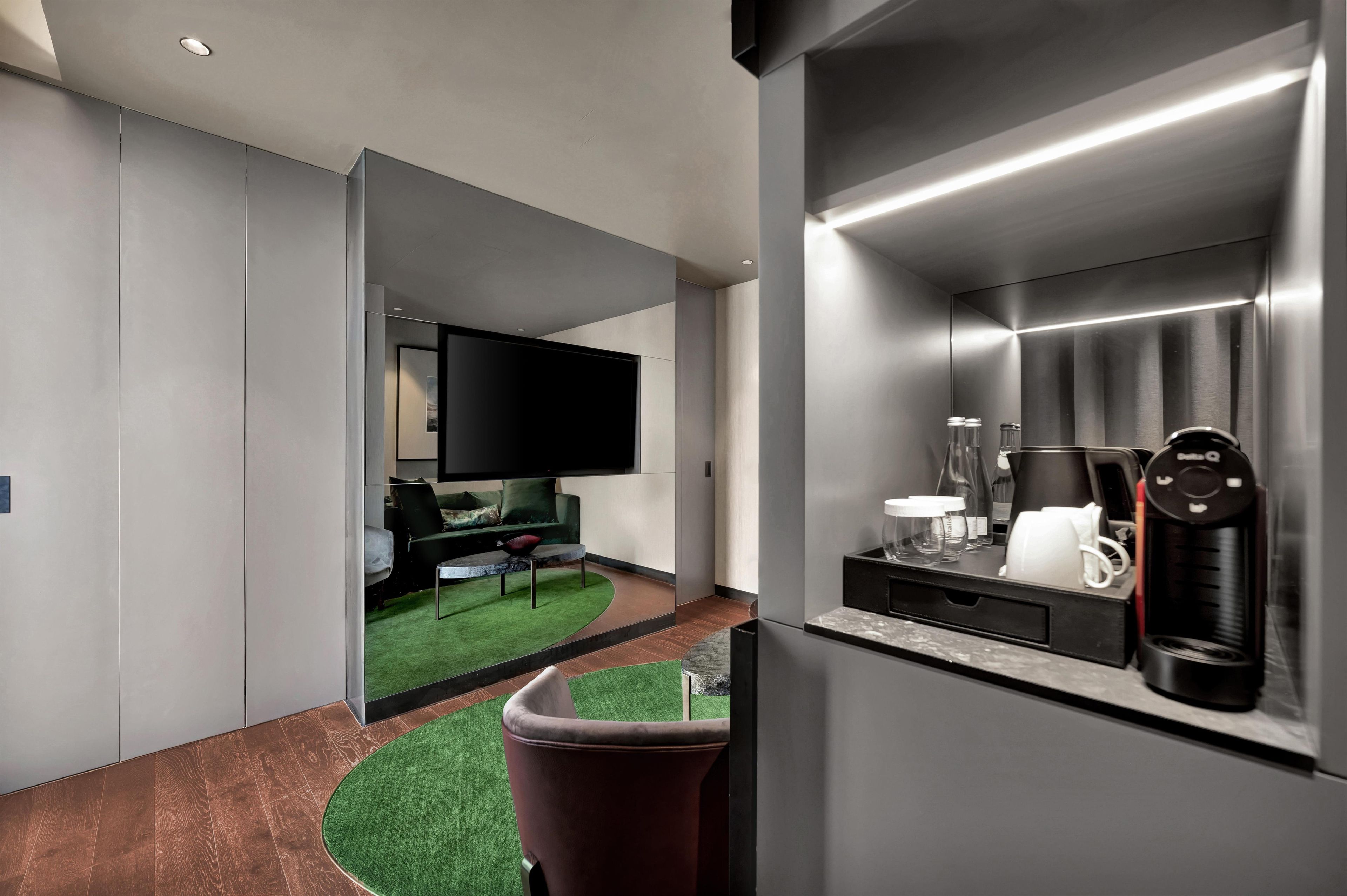 Un interior moderno con una televisión de pantalla plana, una cafetera y una zona de estar con alfombra verde.