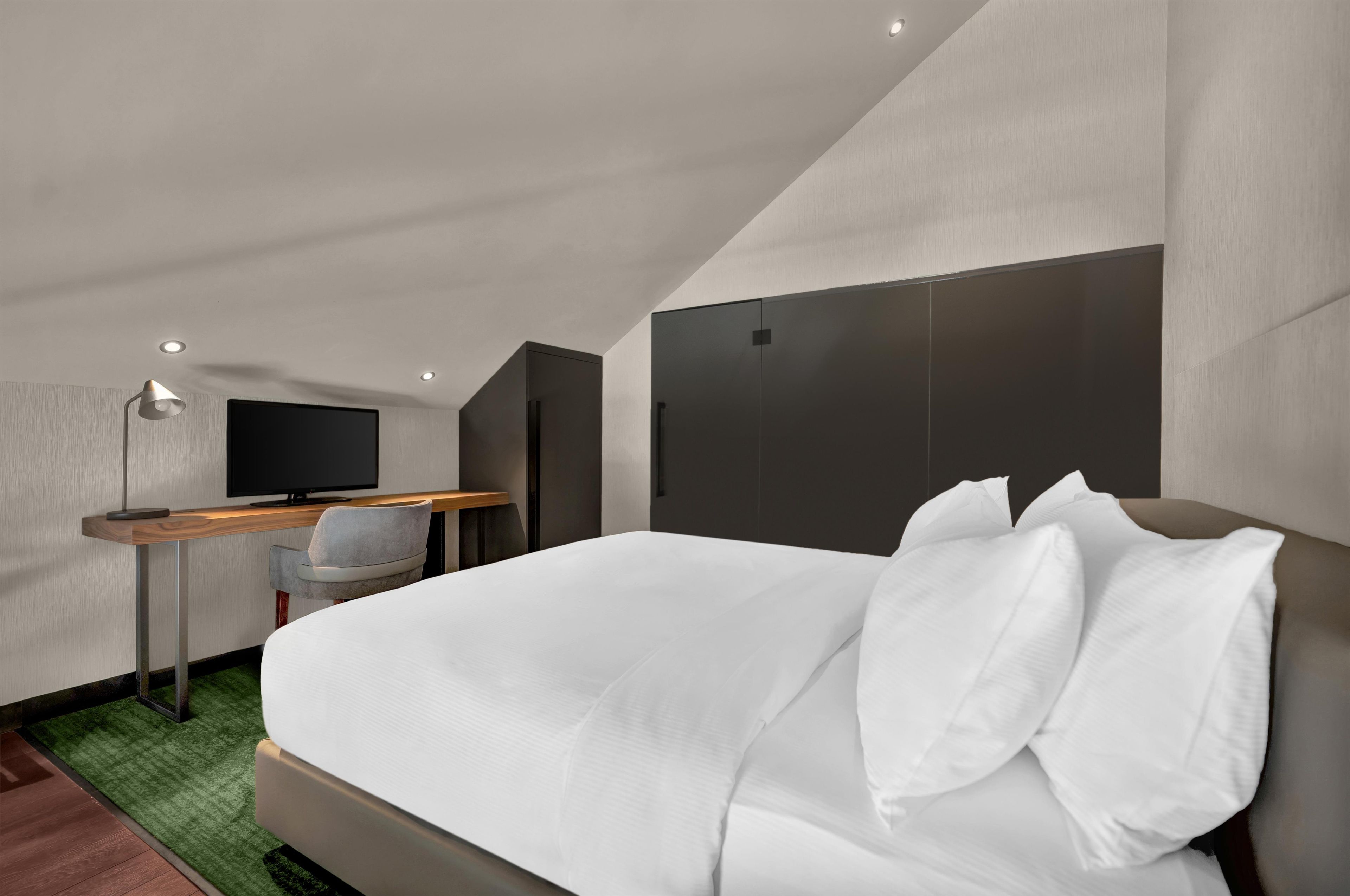 A modern hotel room with a bed, a desk, a chair, and a television.