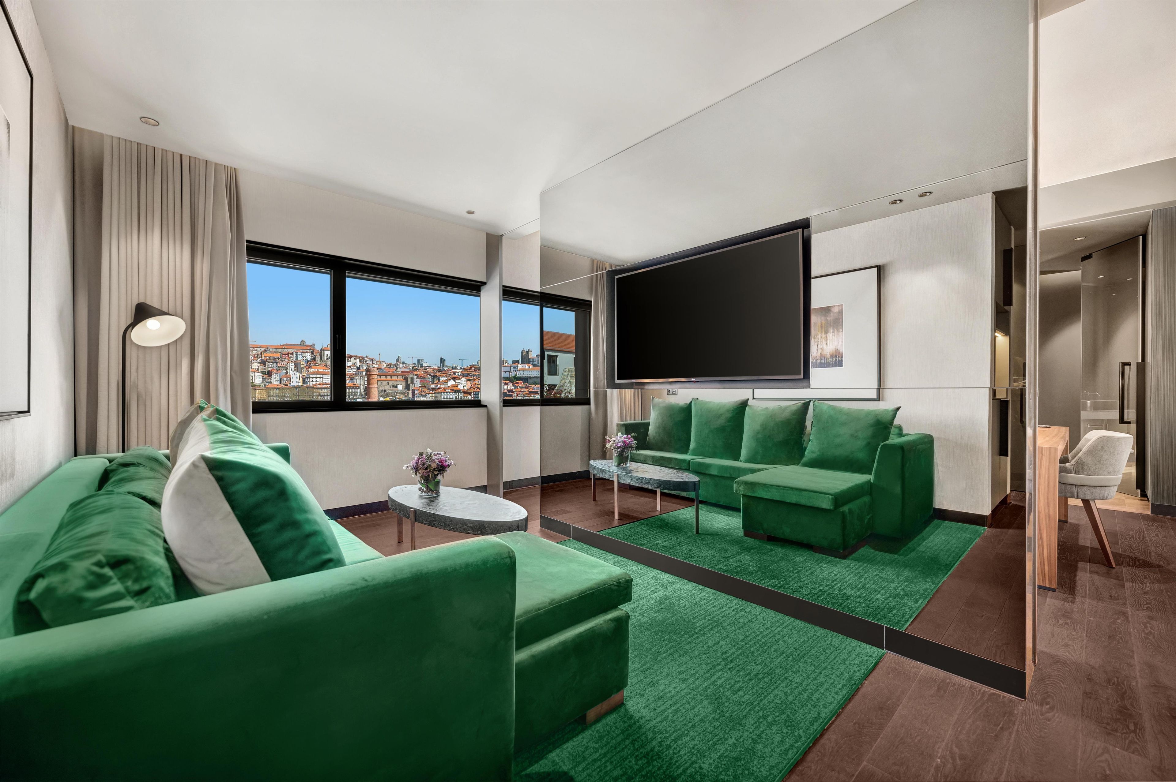 A modern living room with green sofas, a flat-screen TV, and a city view.