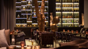 A bar area with a wall of liquor bottles, wooden furniture, and candle-lit tables.