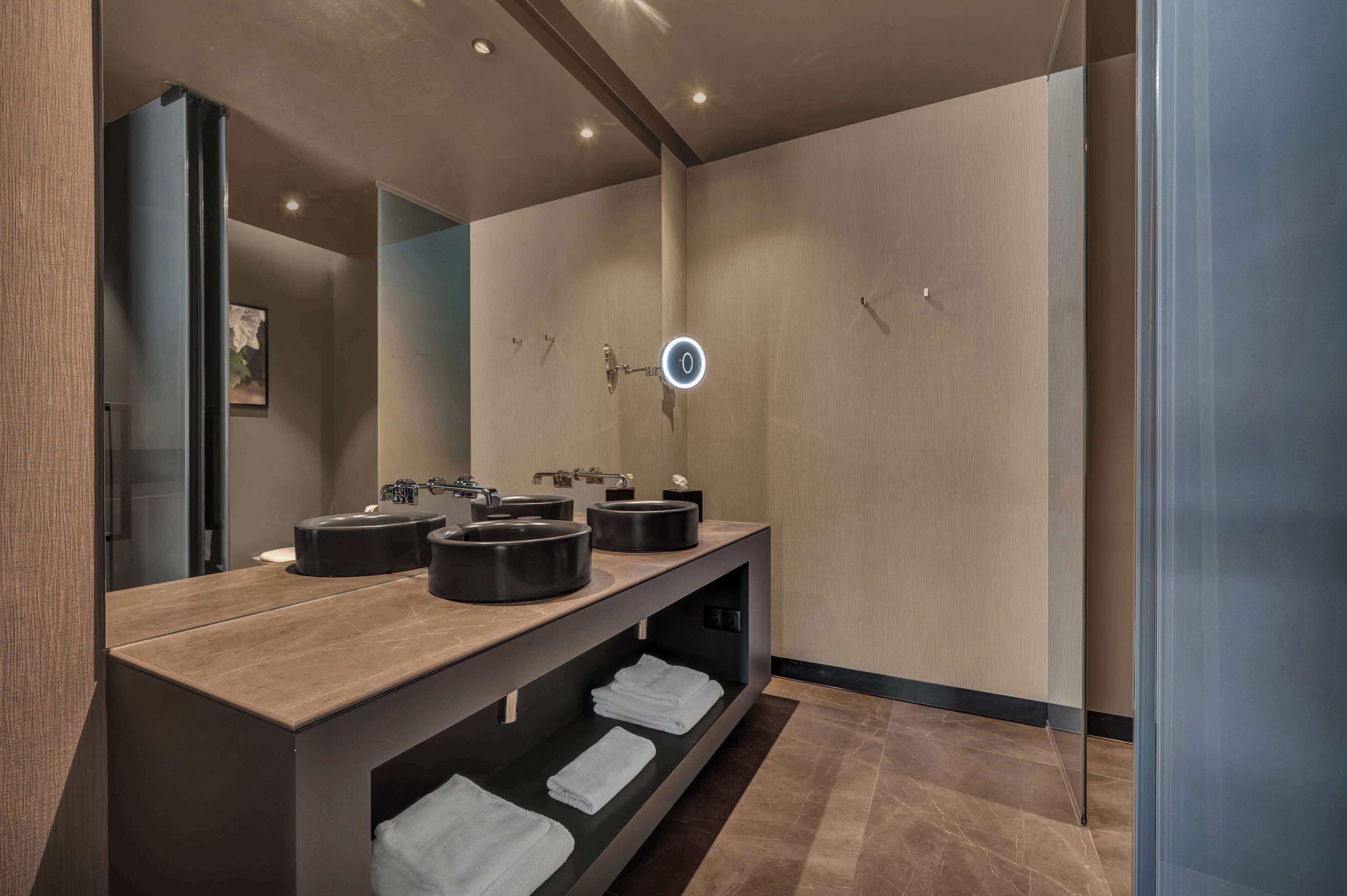 A modern bathroom with a wooden vanity, two black sinks, a mirror, and a towel rack.