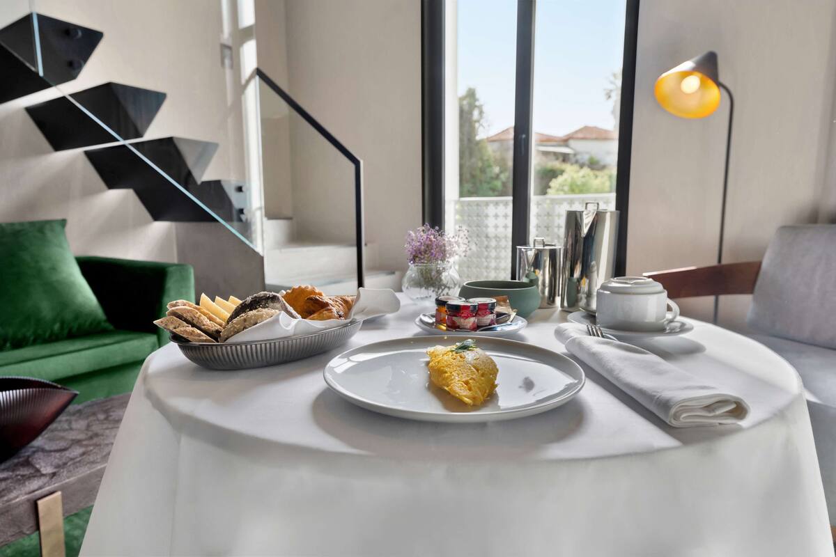 A dining table with a plate of food, a bowl of bread, and a vase of flowers.