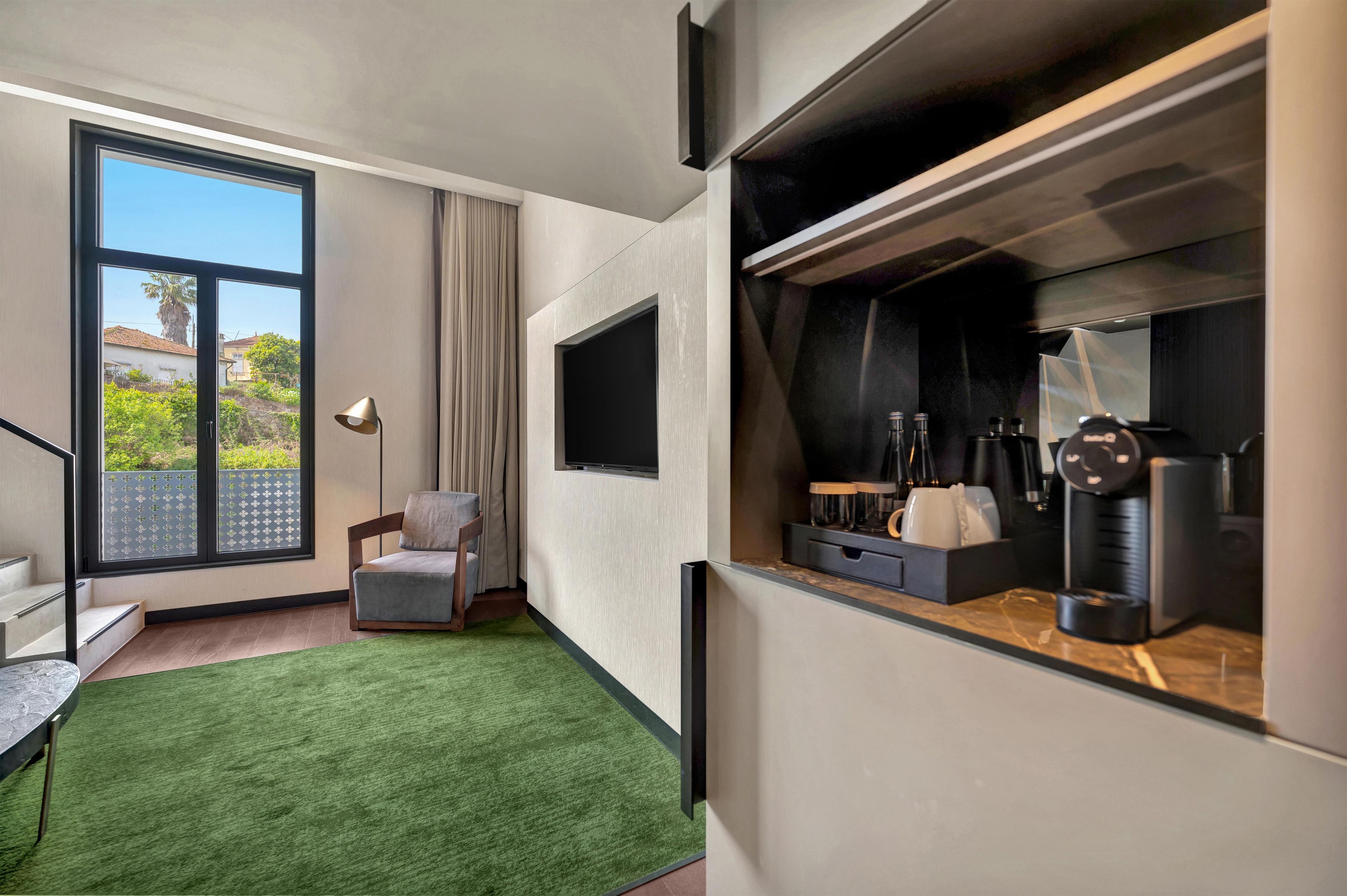 A modern room with a large window, a flat-screen TV, a seating area with a chair, and a coffee machine.