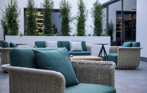 A modern outdoor seating area with wicker furniture and green cushions. - Hilton Porto Gaia (Vila Nova de Gaia)