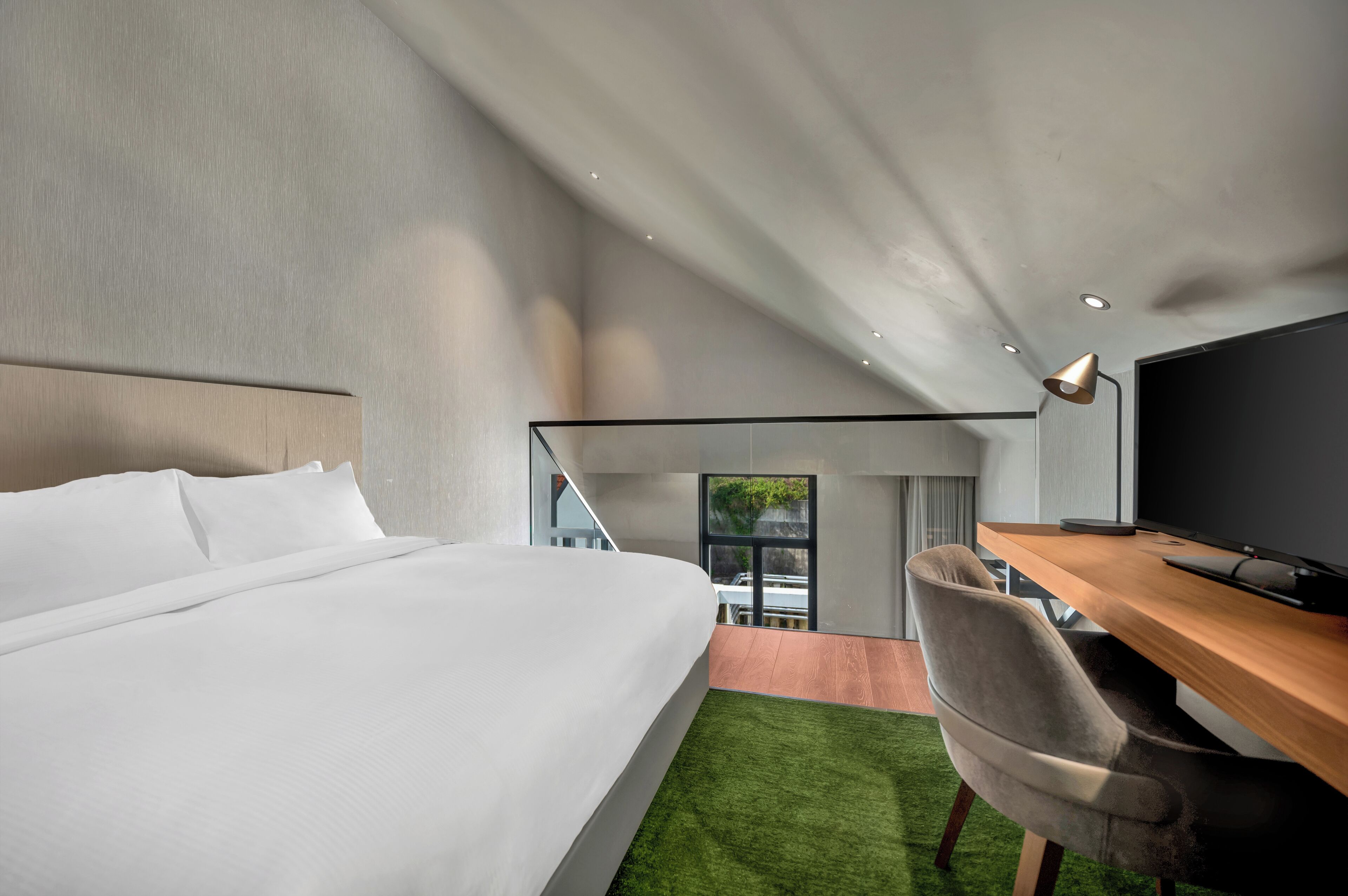 Habitación de hotel moderna con una cama grande, un escritorio con computadora y vistas al exterior.