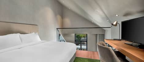 Habitación de hotel moderna con una cama grande, un escritorio con computadora y vistas al exterior.