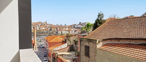 Une vue depuis un balcon donnant sur un paysage urbain, avec des bâtiments historiques et un ciel bleu dégagé.