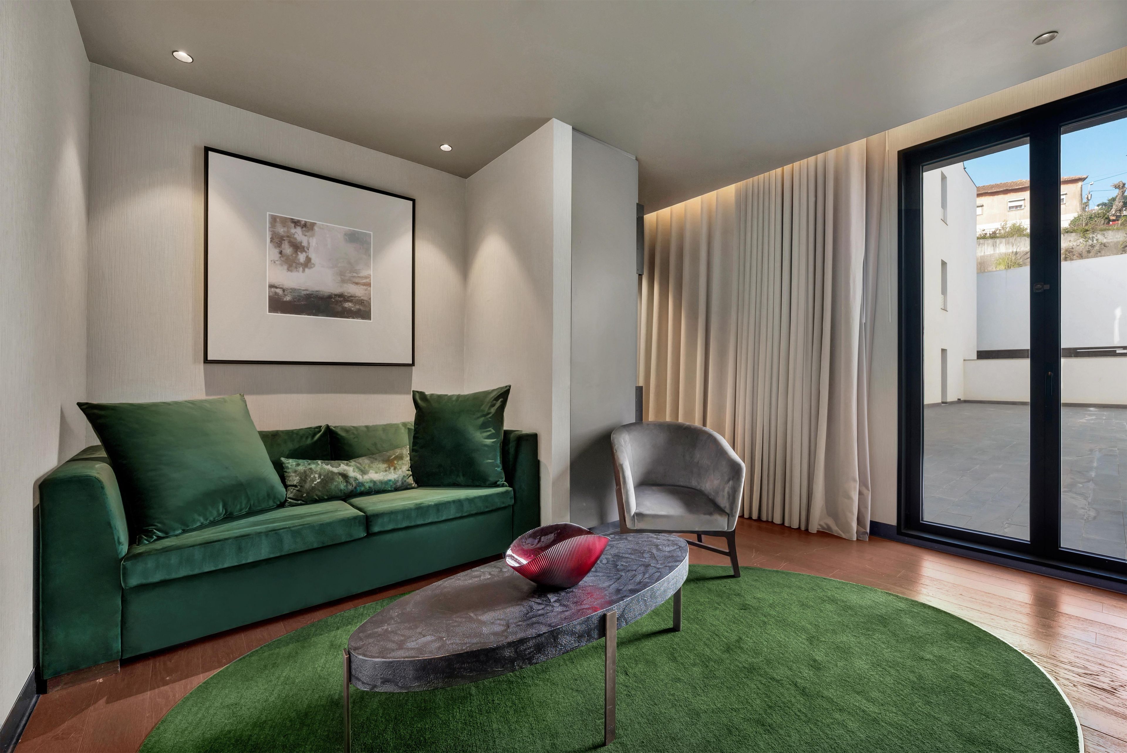 A modern living room with a green sofa, a grey armchair, a small round table, and a large window with curtains.