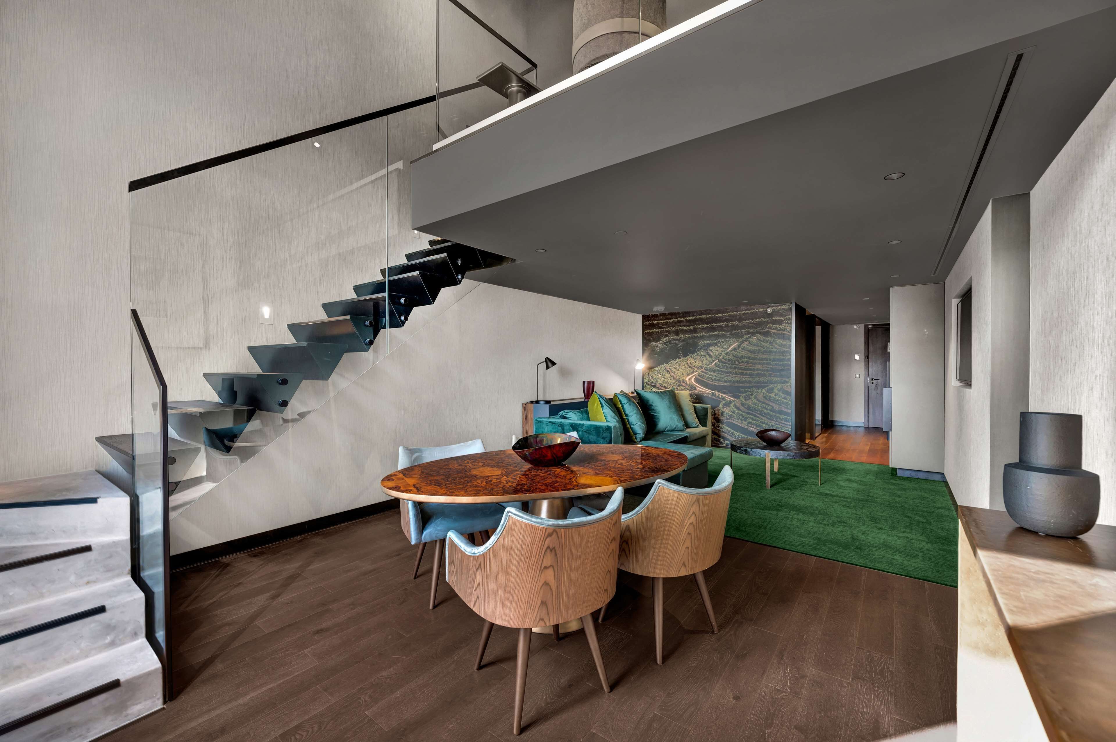 A modern interior with a dining area featuring a round table and chairs, a staircase, and a living area with a green carpet and a sofa.