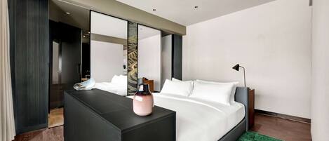 Ein modernes Hotelzimmer mit einem großen Bett, einer dunkelholzigen Kommode, einem grünen Teppich und einem großen Spiegel, der den Raum reflektiert.