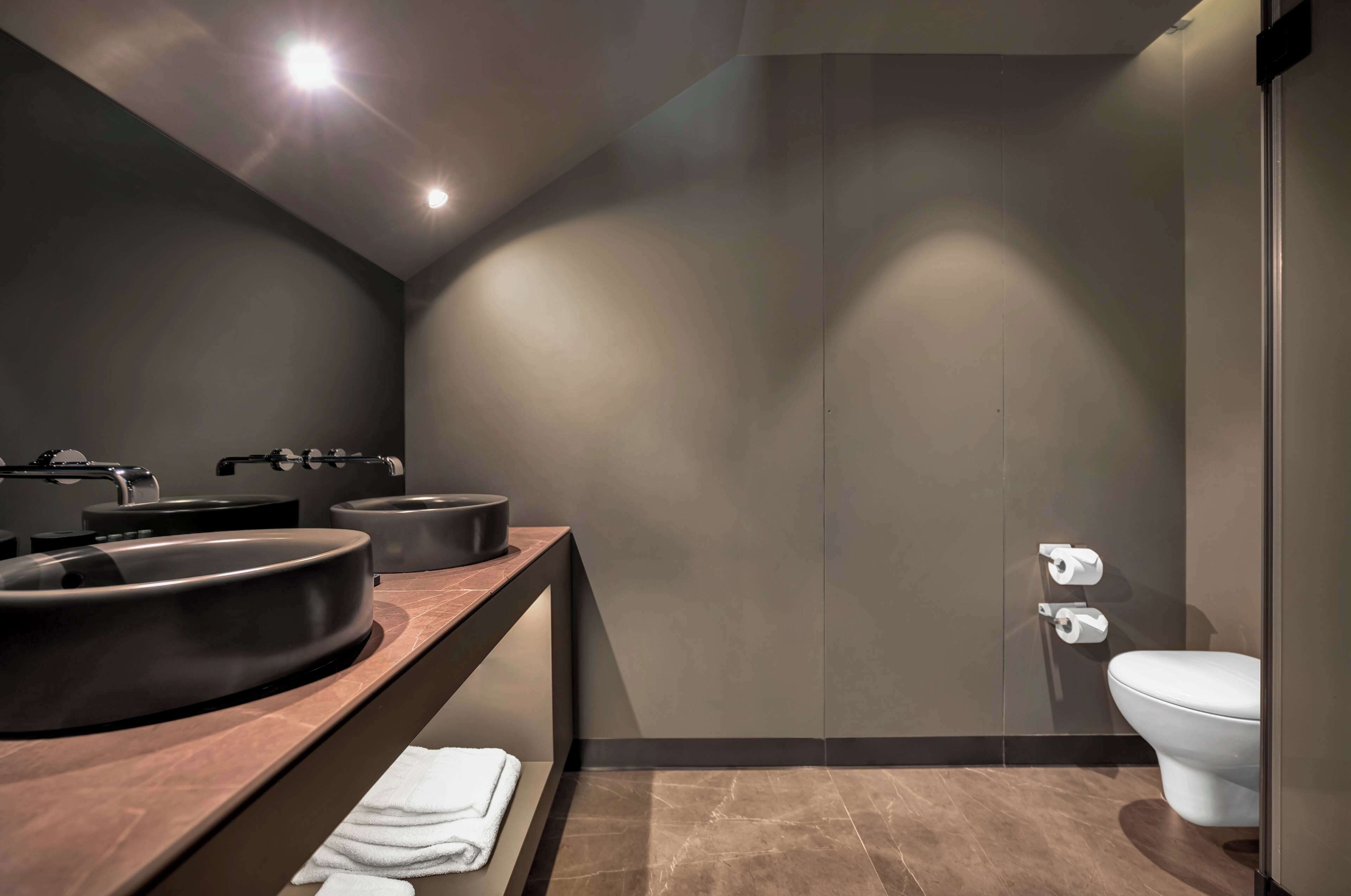 Un baño moderno con una pared oscura, un lavabo redondo, un inodoro y un perchero para toallas.