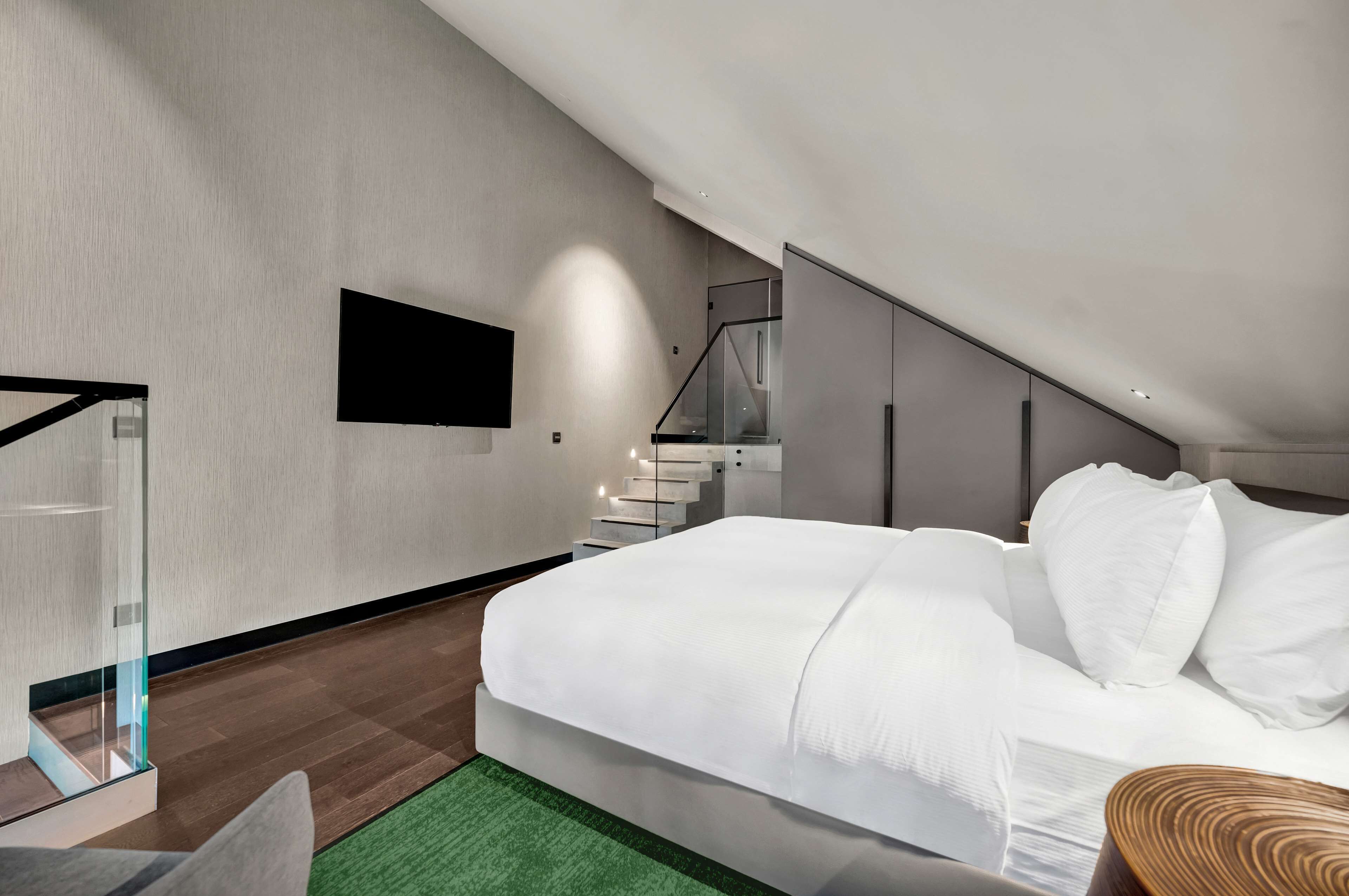 A modern bedroom with a large bed, a staircase, and a flat-screen TV mounted on the wall.