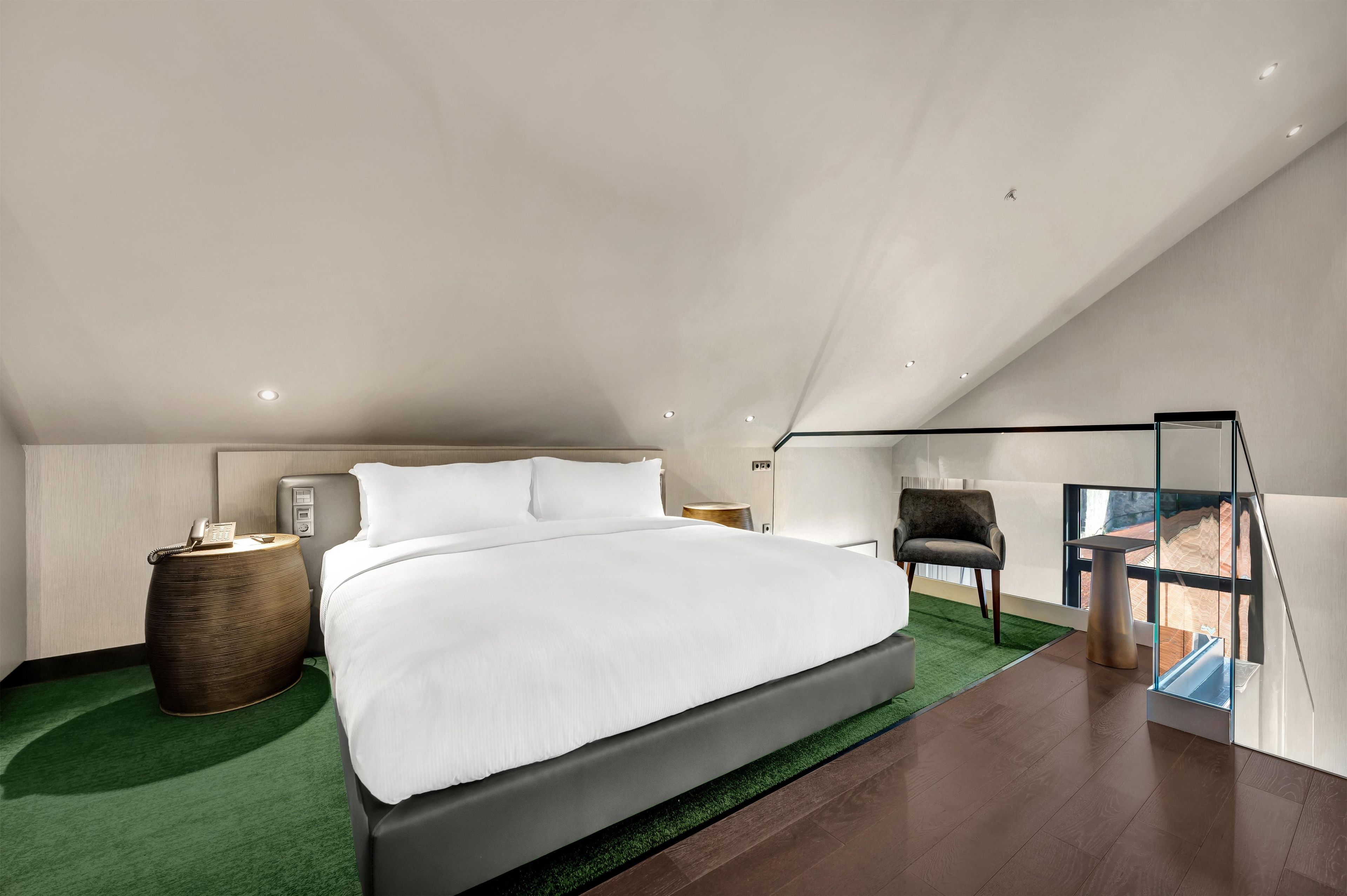 Un dormitorio moderno con una cama grande, una mesita de noche con lámpara, una silla y vistas al exterior a través de un ventanal.