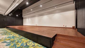 A spacious room with a large wooden stage, a patterned carpet, and a high ceiling with track lighting.