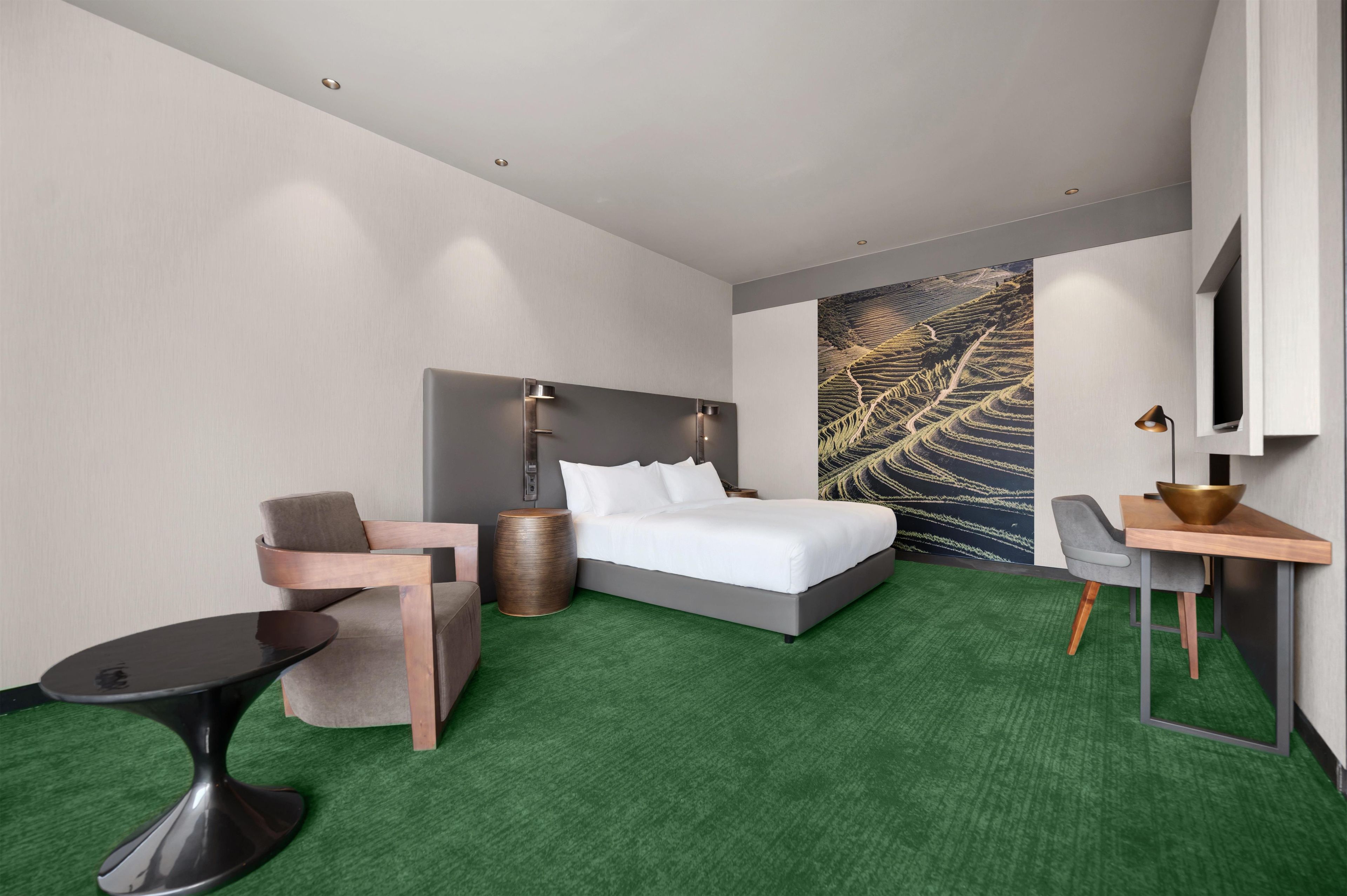 A hotel room with a bed, a chair, a small table, and a wall-mounted TV.