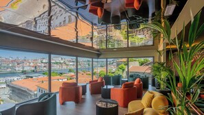 Un salón moderno con asientos cómodos, amplios ventanales que ofrecen vistas de la ciudad y plantas de interior.
