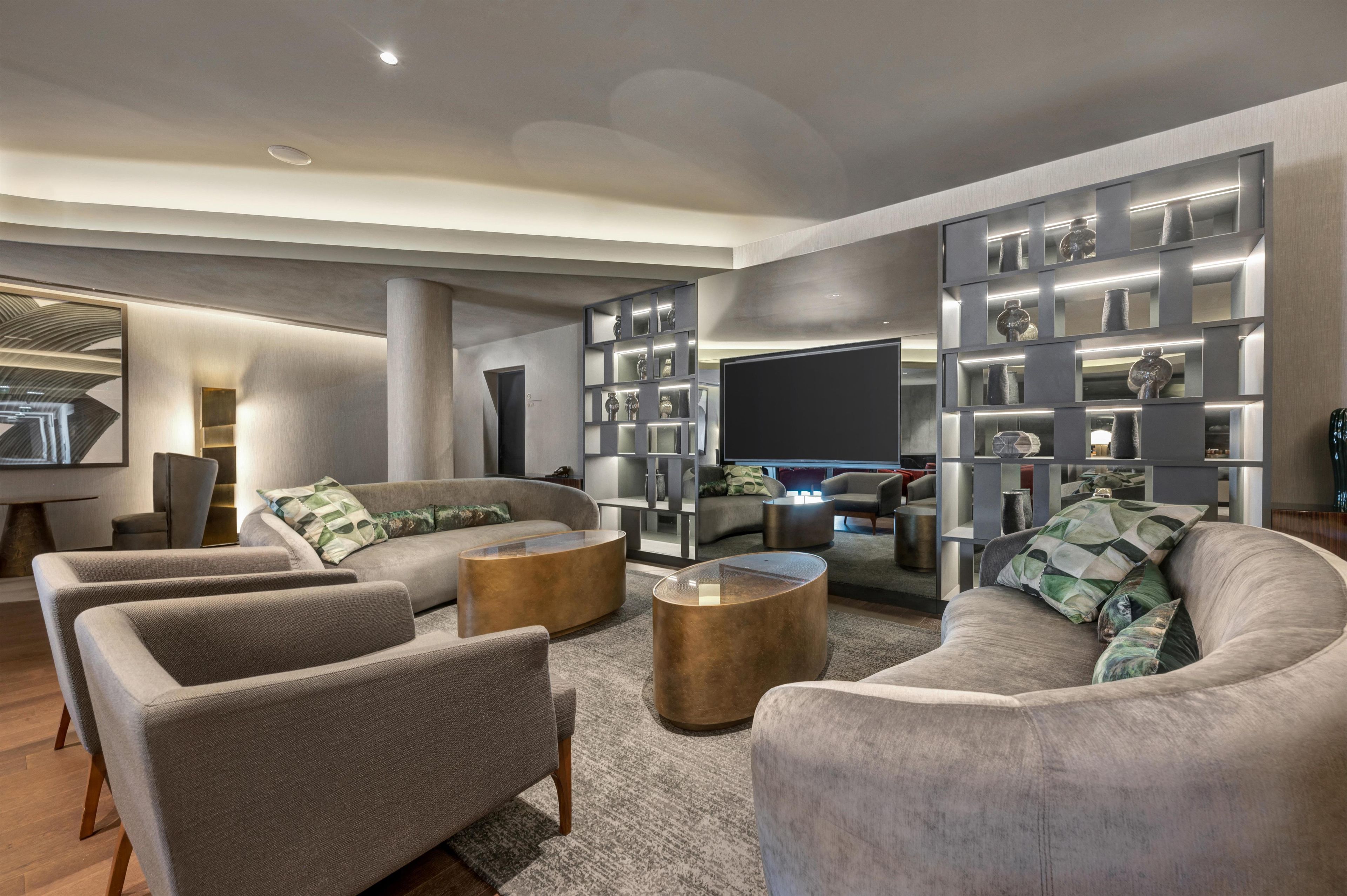 A modern living room with a sectional sofa, two armchairs, a coffee table, and a built-in bookshelf with decorative items.