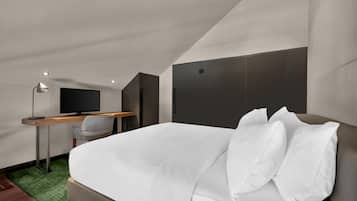 Una habitación de hotel moderna con cama, escritorio, silla, televisor y alfombra verde.