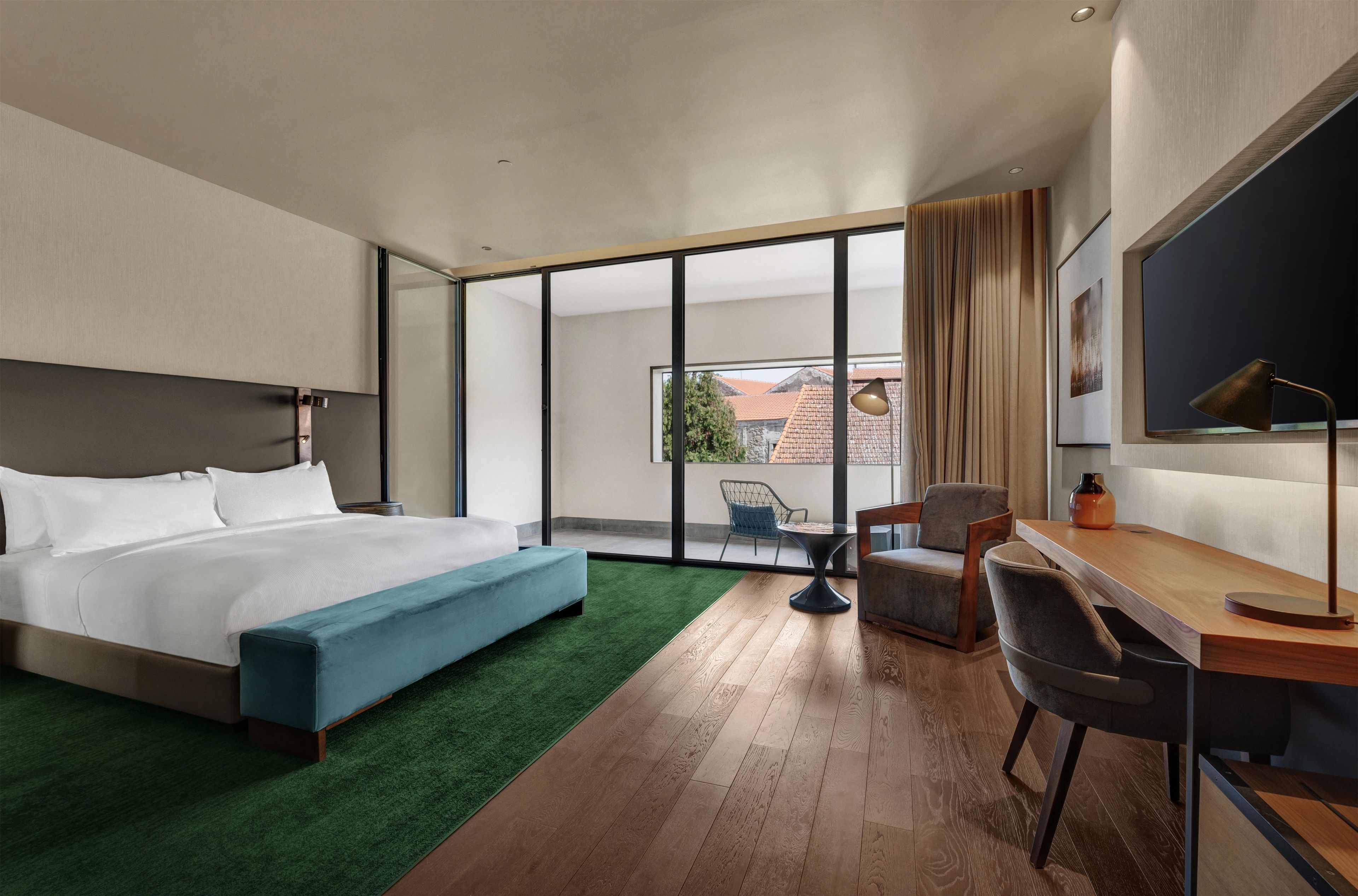 Habitación de hotel moderna con una cama grande, un escritorio, una silla y vistas al exterior.