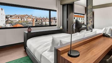 Una habitación de hotel moderna con una cama grande, un escritorio de madera y vistas a un paisaje urbano.