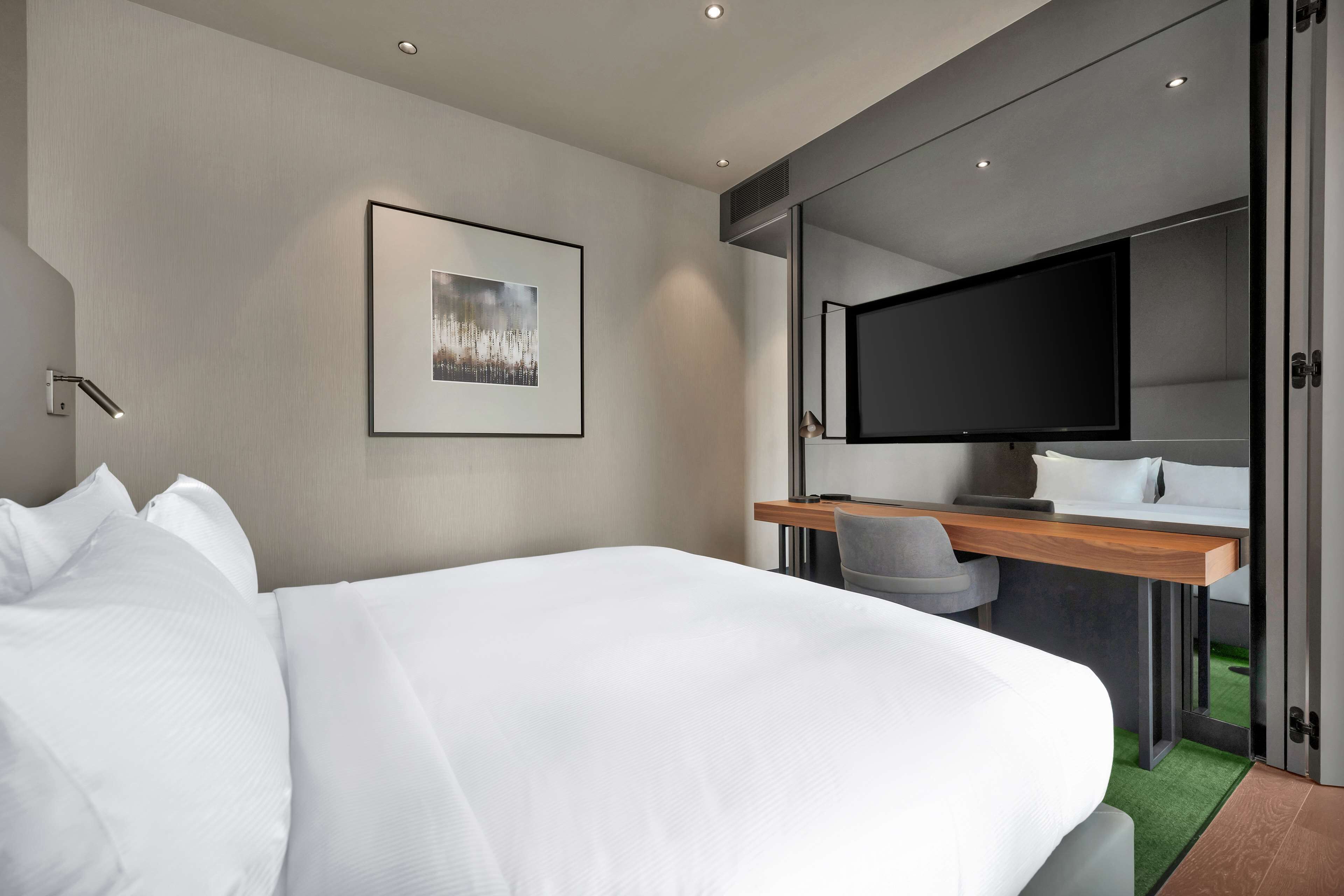 Een moderne hotelkamer met een groot bed, een bureau met een flatscreen televisie en een ingelijst schilderij aan de muur.