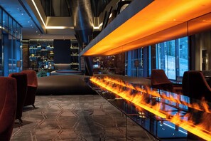 A modern hotel lobby with a glass partition, seating area, and a fire feature. - Hilton Porto Gaia (Vila Nova de Gaia)