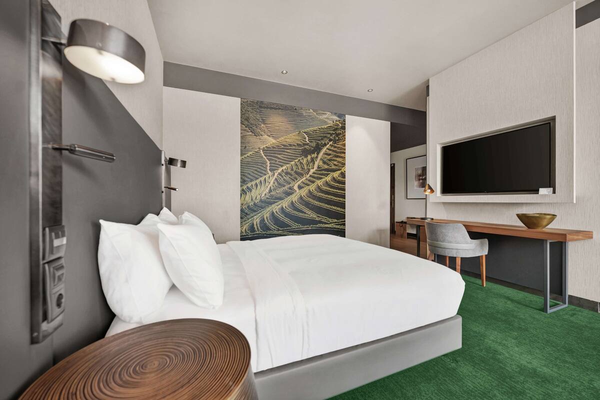 A modern hotel room with a large bed, a desk, a flat-screen TV, and a wall-mounted artwork.