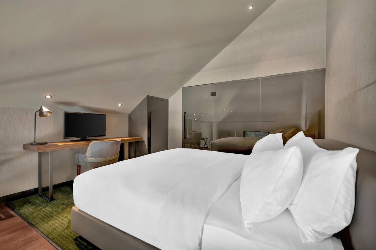 A modern hotel room with a large bed, a desk with a flat-screen TV, and a chair.