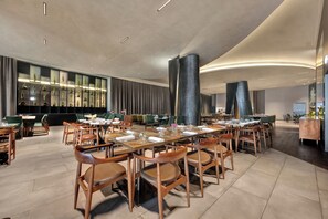A spacious dining area with multiple tables and chairs, a bar with glassware, and a modern ceiling design. - Hilton Porto Gaia (Vila Nova de Gaia)