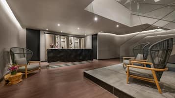 Un vestíbulo moderno con mostrador de recepción, sillas de mimbre y suelo de madera.