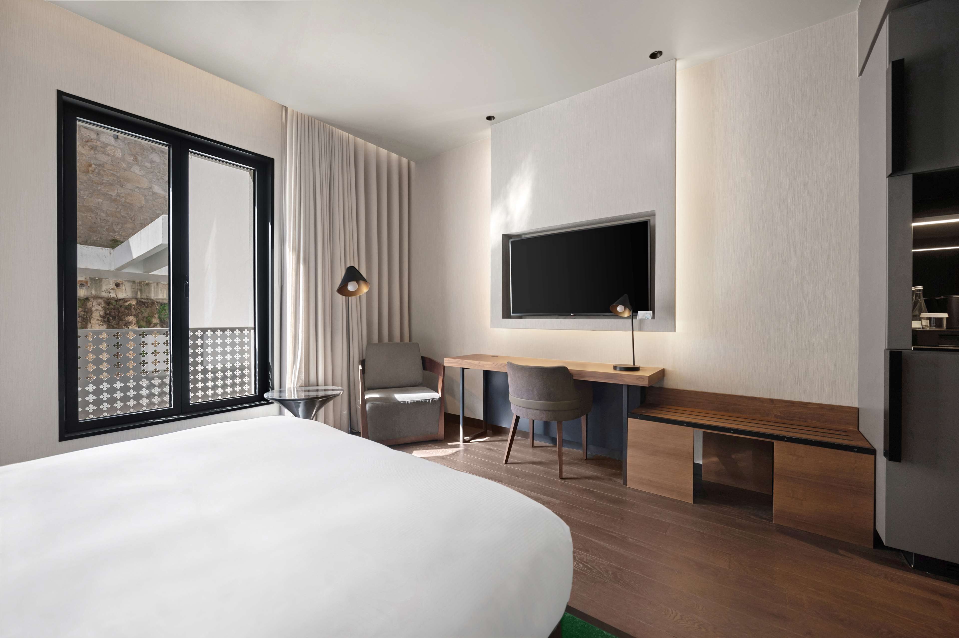 Una habitació d'hotel moderna amb un llit gran, un escriptori amb dues cadires, un televisió de pantalla plana i una nevera.