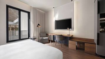 Een moderne hotelkamer met een groot bed, een bureau met twee stoelen, een flatscreen televisie en een minibar.