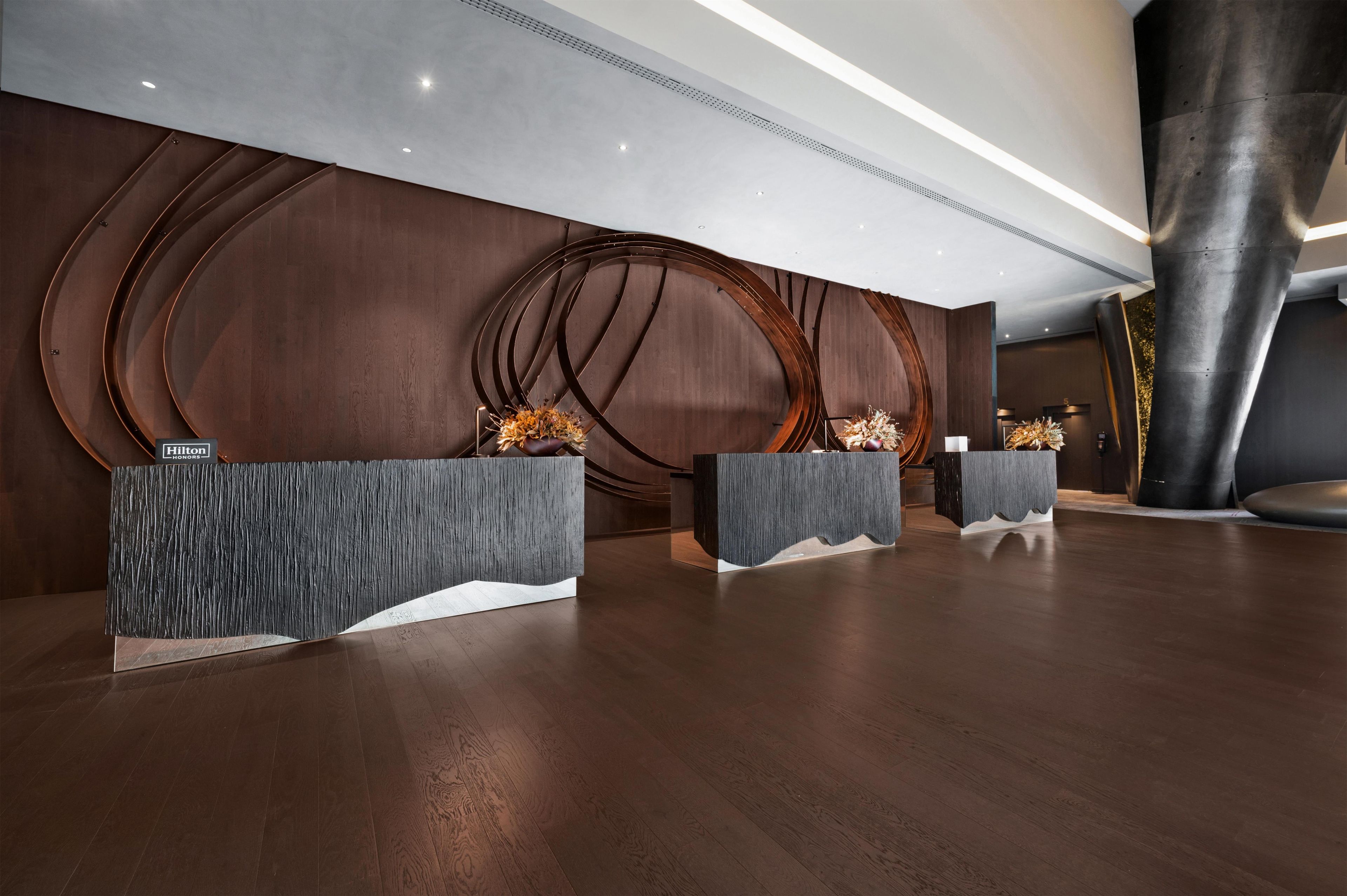A modern reception area with three dark wooden reception desks, each with a unique design and a floral arrangement.