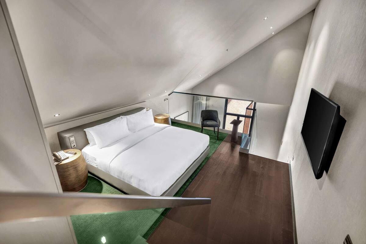 A modern bedroom with a large bed, a chair, a TV, and a small table.