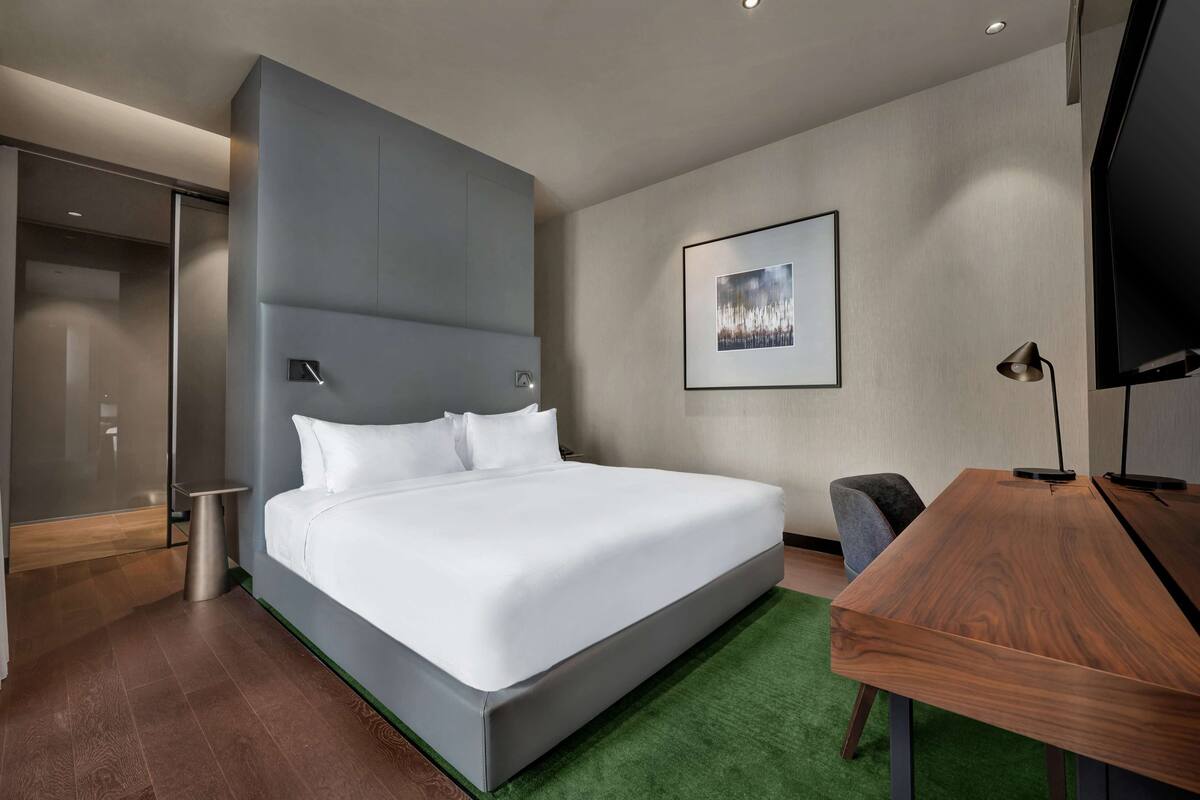 A modern hotel room with a large bed, a desk, and a television.