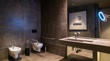 A modern bathroom with a bidet, toilet, vanity with a mirror, and a framed picture on the wall.